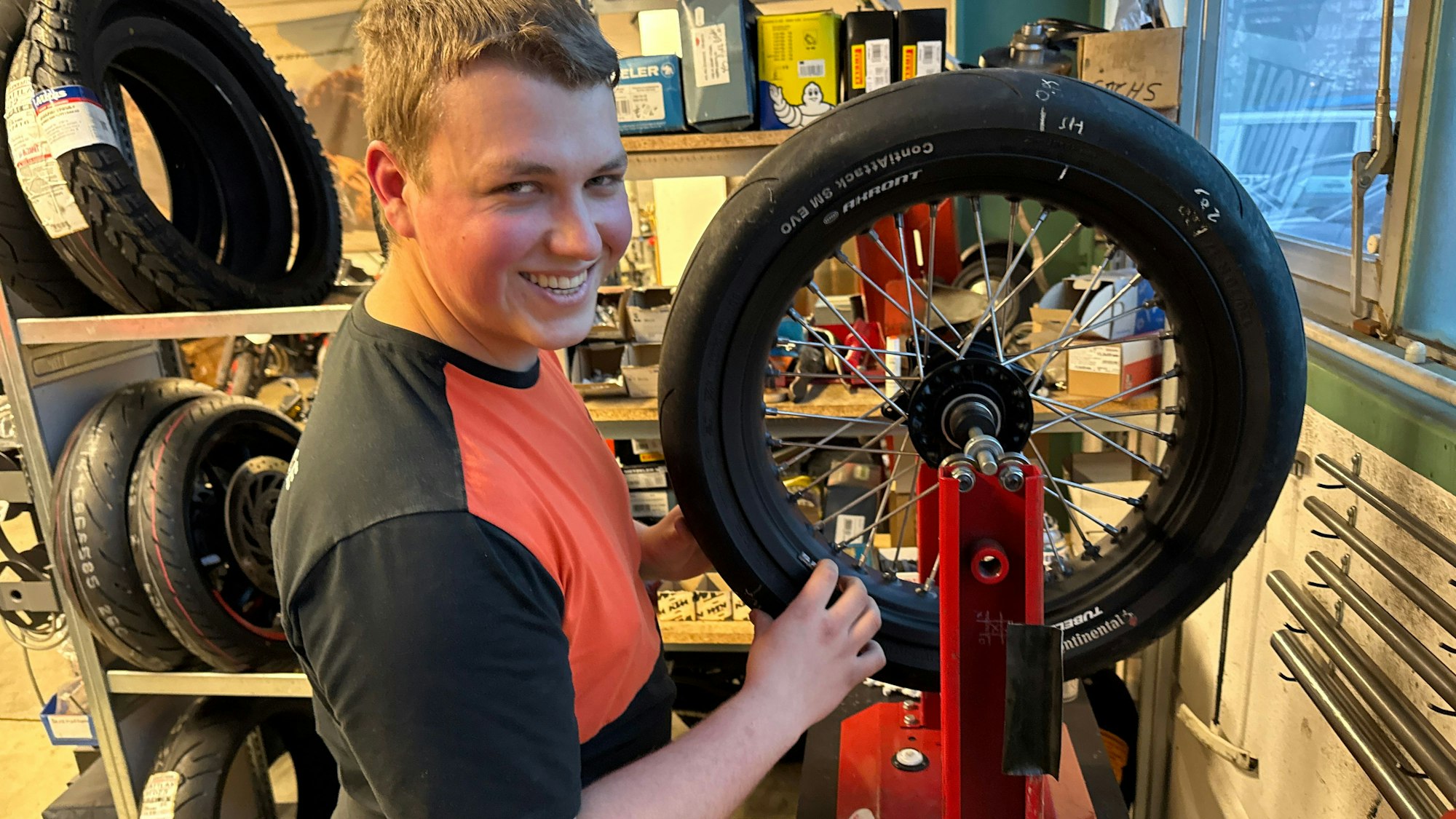 Ein junger Mann hantiert mit einem Motorradreifen.