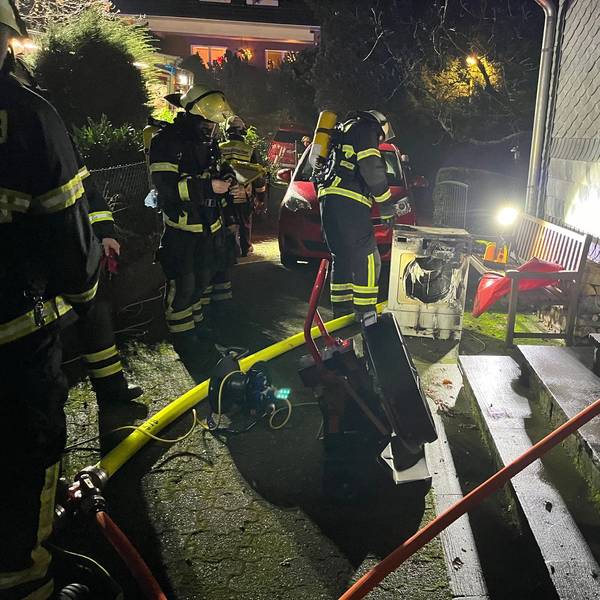 Einsatzkräfte löschen einen verschmorten Wäschetrockner vor einem Haus.