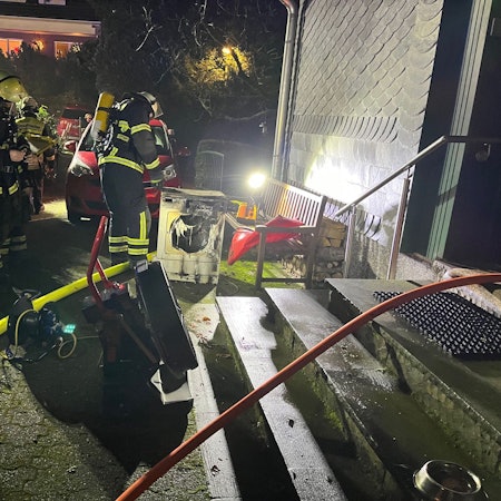 Einsatzkräfte löschen einen verschmorten Wäschetrockner vor einem Haus.