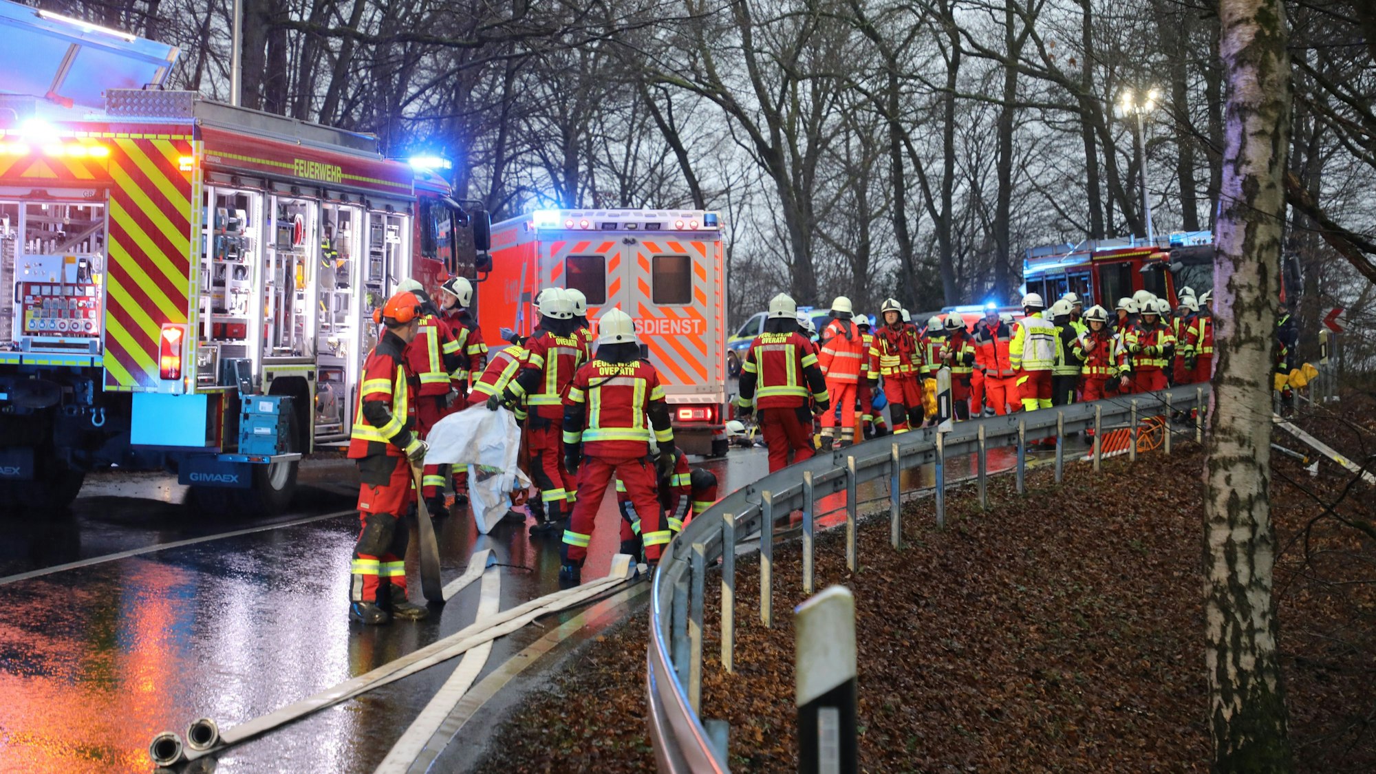 Feuerwehrleute, Rettungsdienst und Polizisten stehen mit zahlreichen Fahrzeugen auf der Mucher Straße bei Overath.