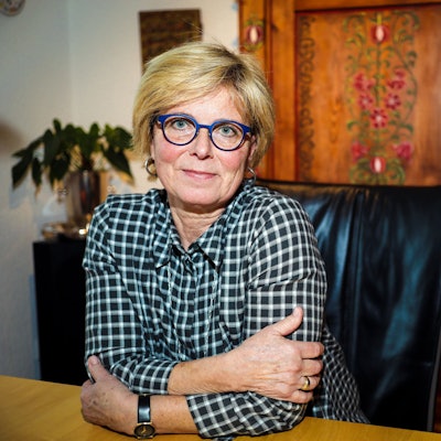 Verena Welschof sitzt zuhause an einem Esstisch und lächelt in die Kamera. Sie sieht frisch und gut aus.