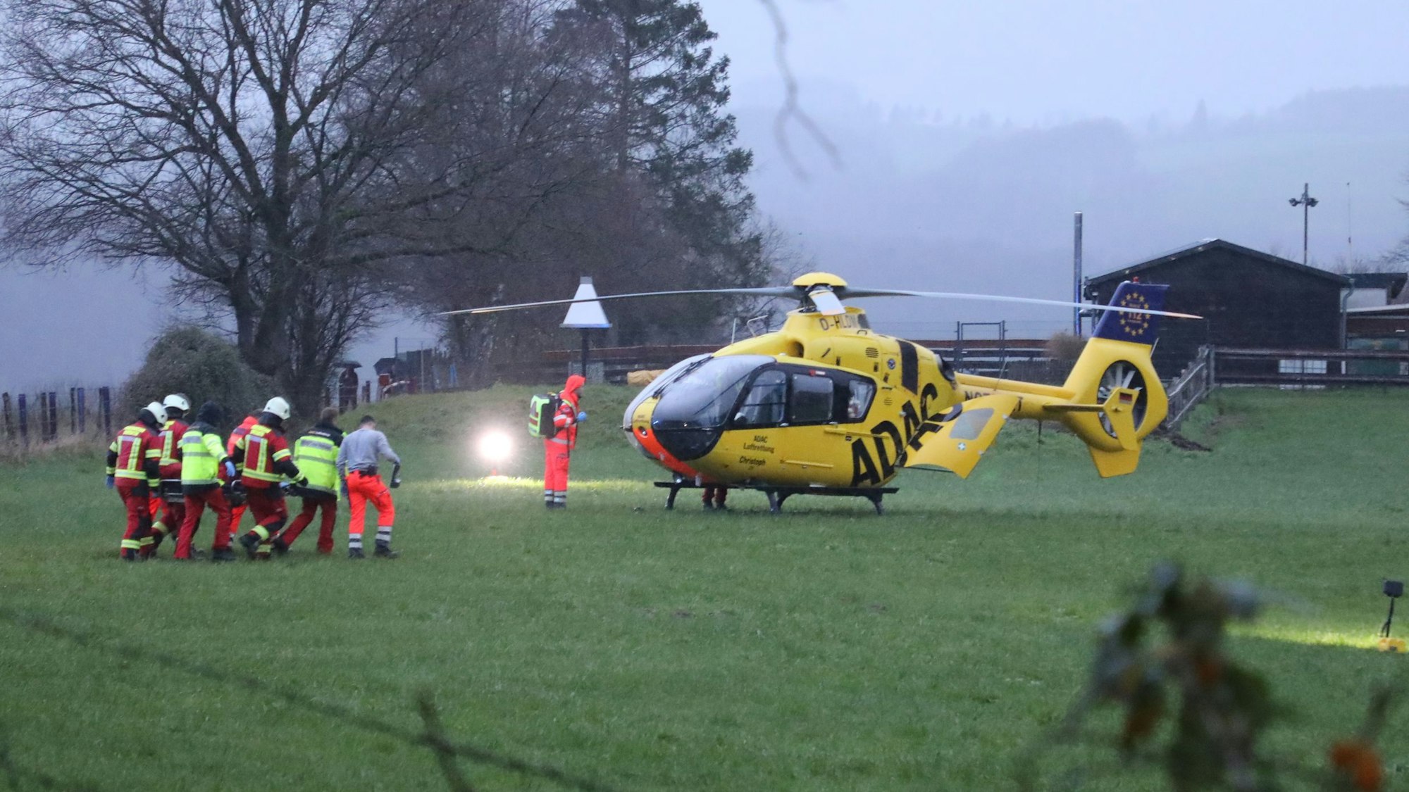 Retter tragen eine Verletzte zu einem Rettungshubschrauber auf einer Wiese.