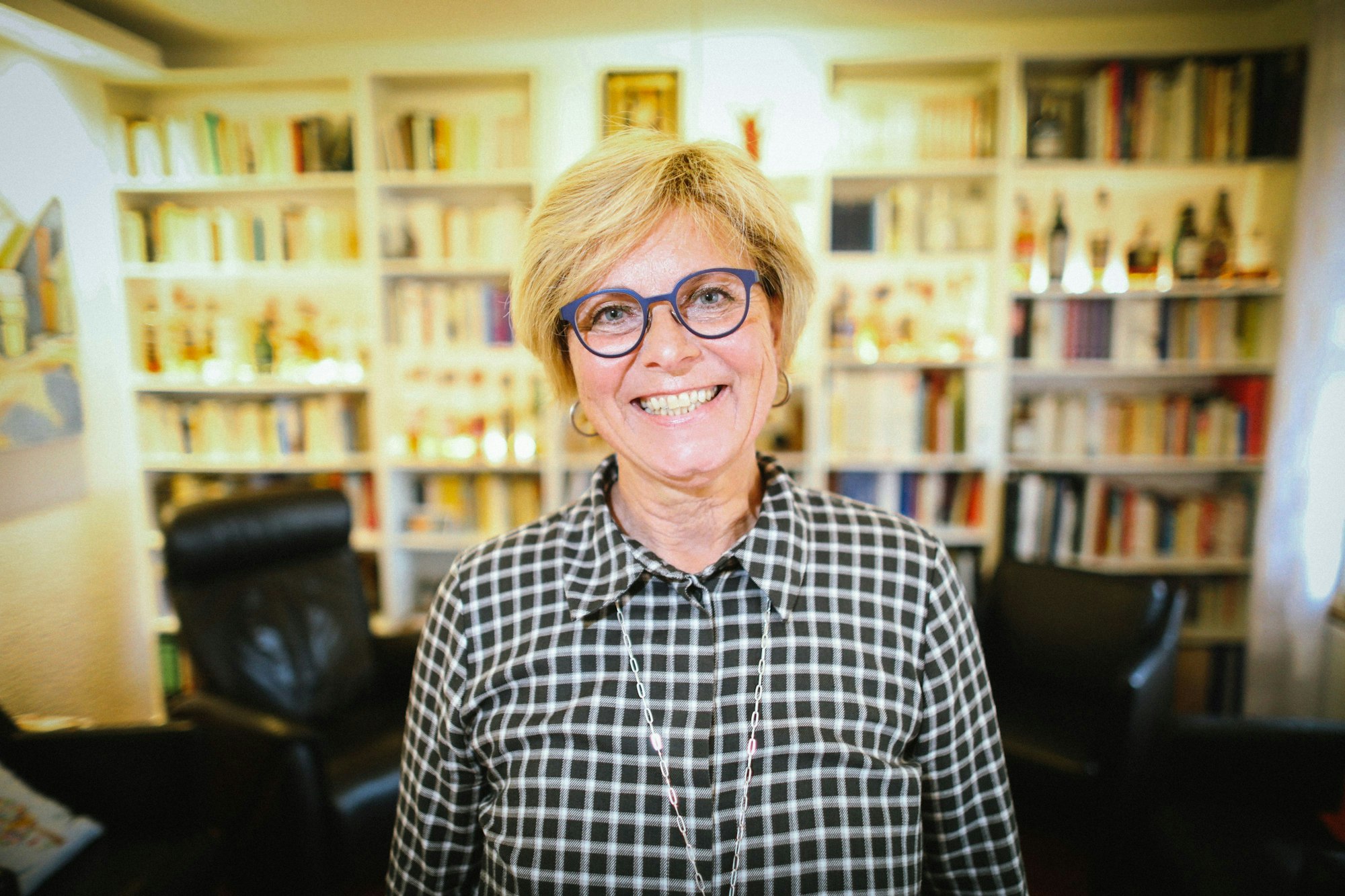 Verena Welschof lacht mit offenem Blick in die Kamera. Hinter ihr ist ein volles Bücherregal zu sehen.