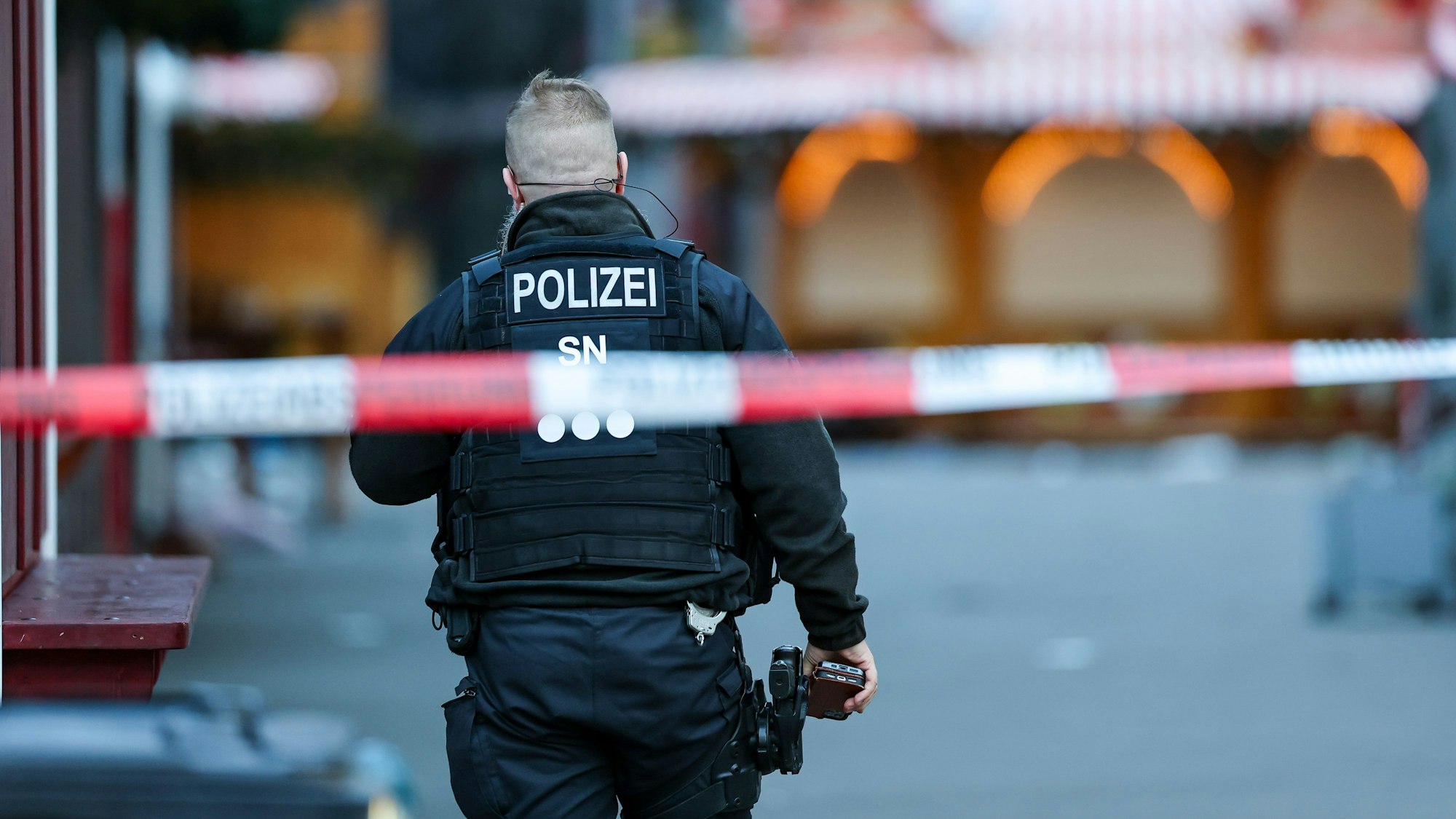 Ein Polizist steht hinter einer Absperrung am Magdeburger Weihnachtsmarkt. Am Vorabend war ein Autofahrer in eine Menschengruppe gefahren. Es gab mehrere Tote und Verletzte.