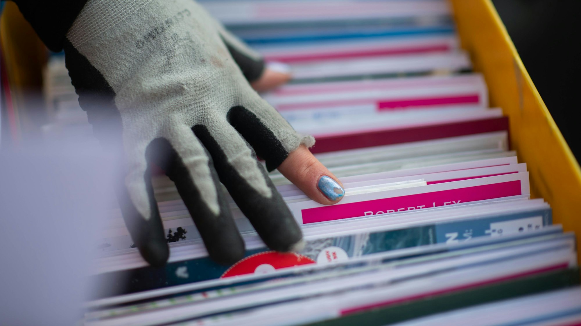 Das Bild zeigt eine Hand. An einem Finder blättert der Nagellack ab. Zudem sind die Fingerkuppen des Handschuhs abgeschnitten.