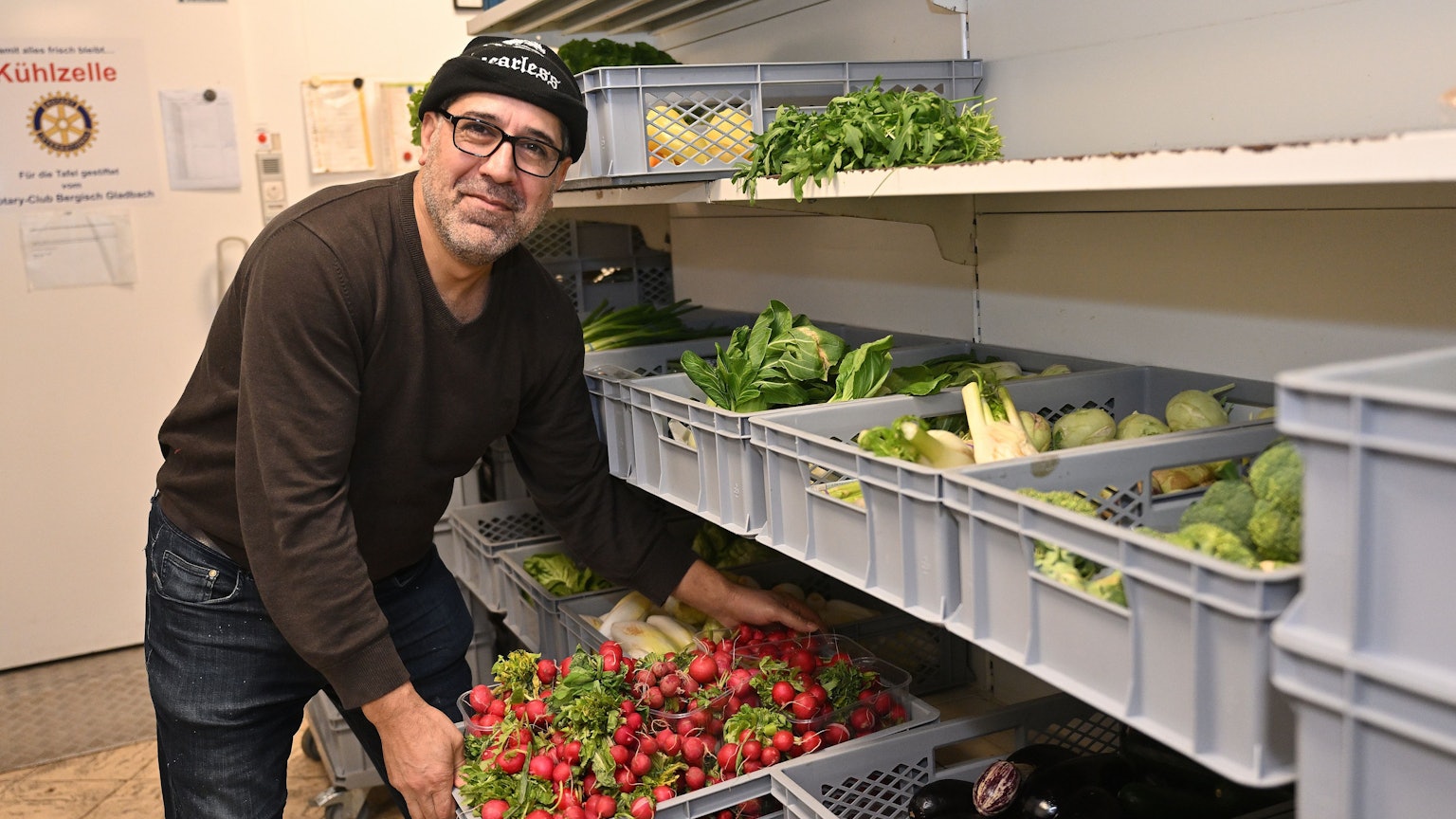 Der Helfer räumt eine Kiste mit Radieschen aus dem Regal.