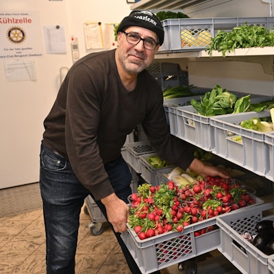 Der Helfer räumt eine Kiste mit Radieschen aus dem Regal.