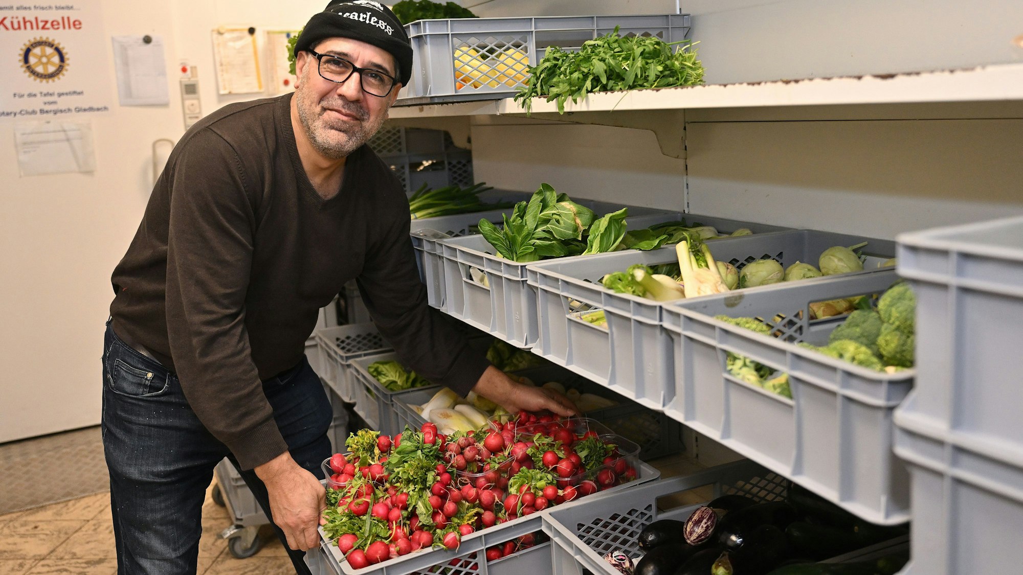Der Helfer räumt eine Kiste mit Radieschen aus dem Regal.