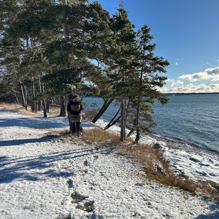 Eine Frau blickt vom verschneiten Ufer aus auf einen großen See.