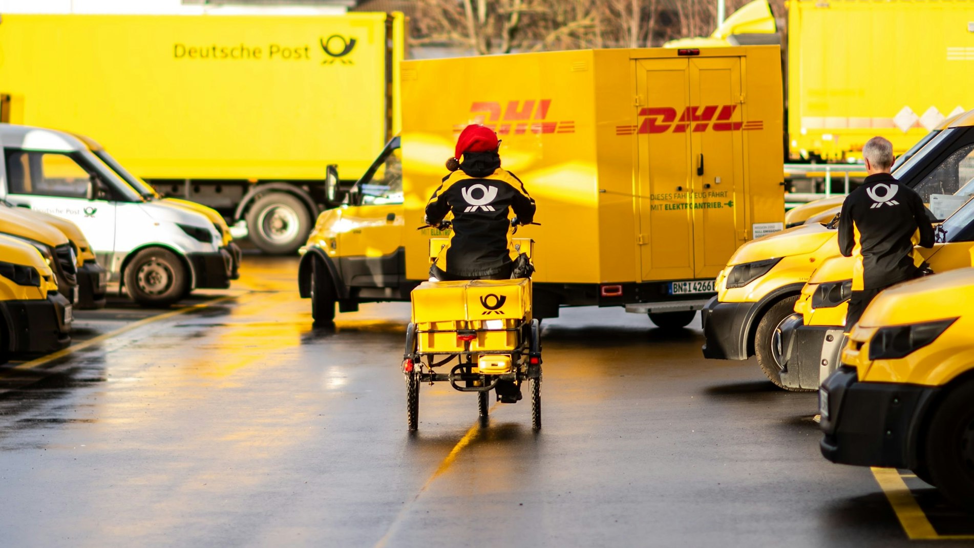 Eine Postmitarbeiterin fährt auf einem Fahrrad. Sie trägt eine rot-weiße Weihnachtsmütze.