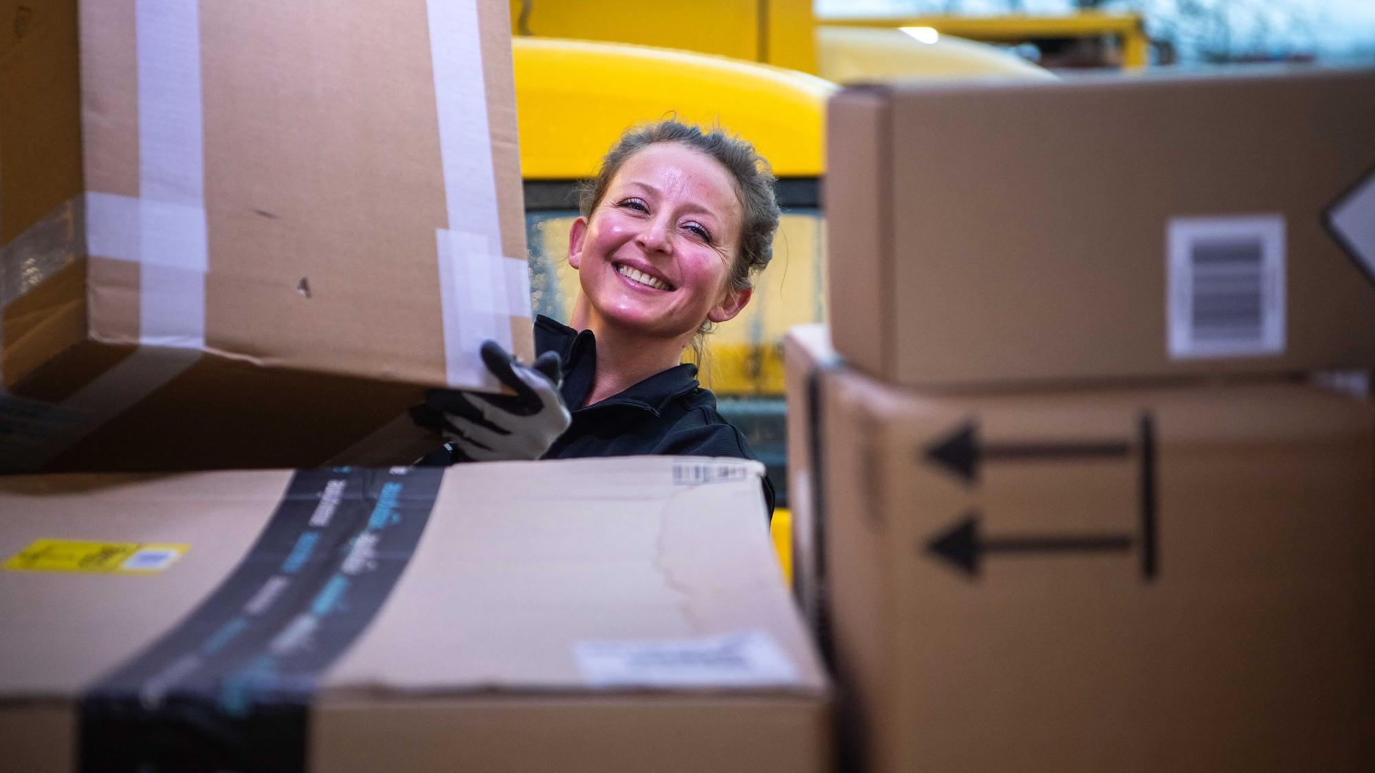 Das Bild zeigt eine Postmitarbeiterin, die ein Paket in ein Zustellfahrzeug lädt.
