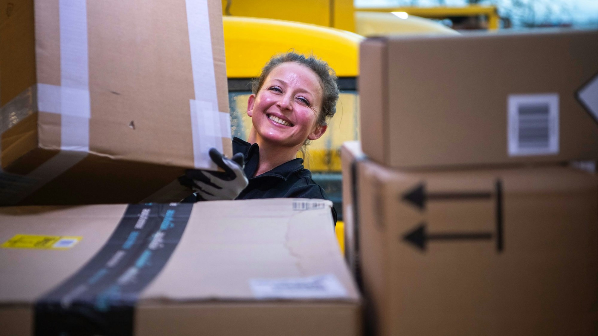 Das Bild zeigt eine Postmitarbeiterin, die ein Paket in ein Zustellfahrzeug lädt.