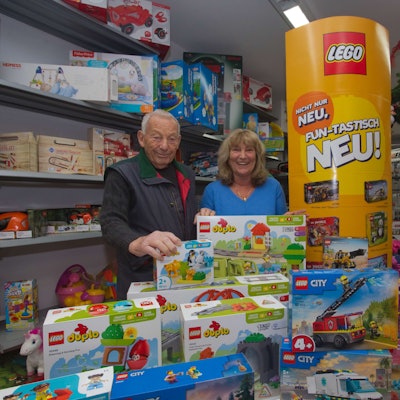 Ein Vater steht mit seiner Tochter hinter einem Tisch mit Spielwaren in deren eigenen Spielzeugladen.