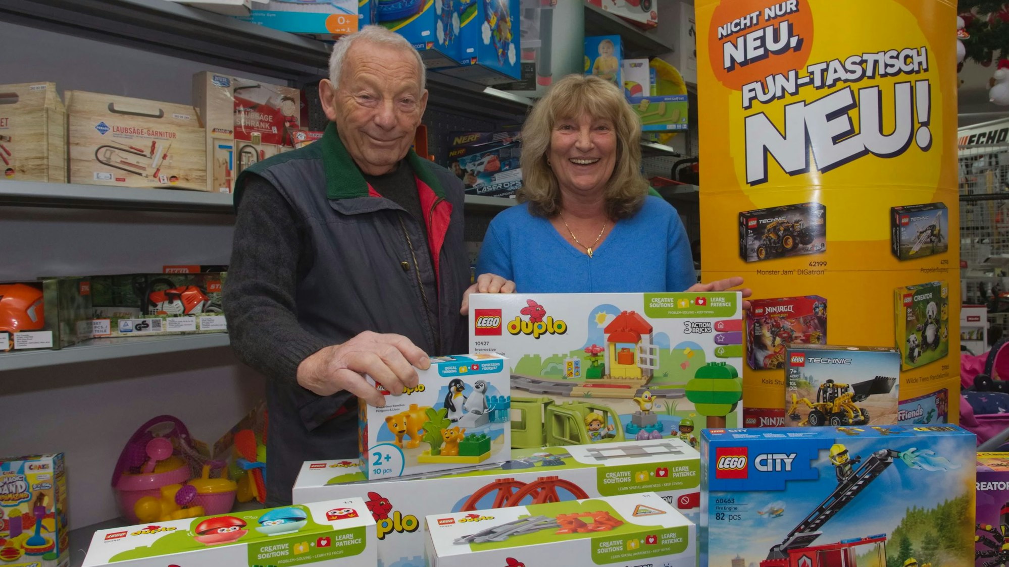 Ein Vater steht mit seiner Tochter hinter einem Tisch mit Spielwaren in deren eigenen Spielzeugladen.