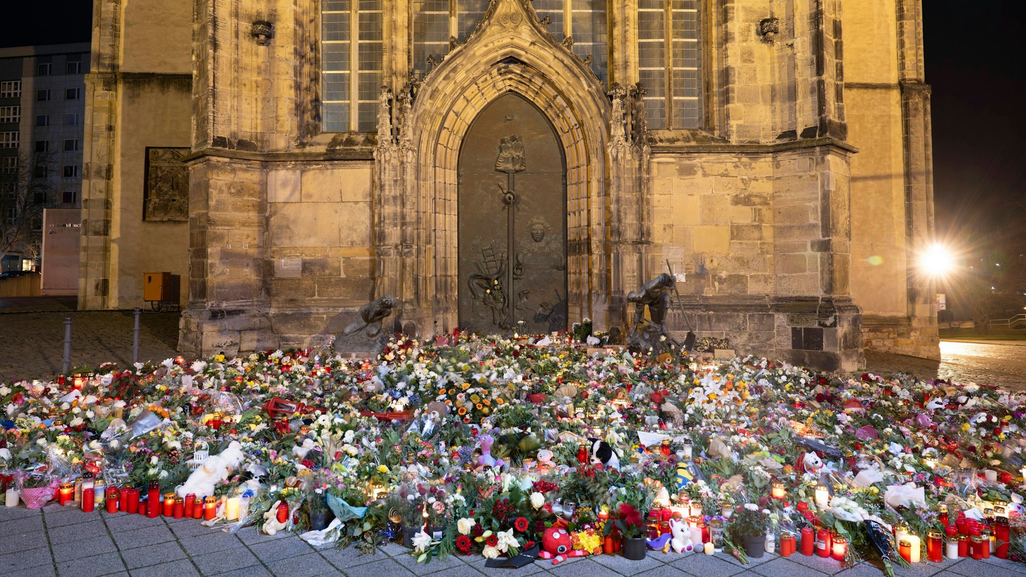 Zahlreiche Kerzen, Blumen und Kränze liegen beziehungsweise stehen vor dem Eingang der Johanniskirche. Am 20. Dezember 2024 ist auf dem Weihnachtsmarkt in Magdeburg ein Autofahrer in eine Menschengruppe gefahren.