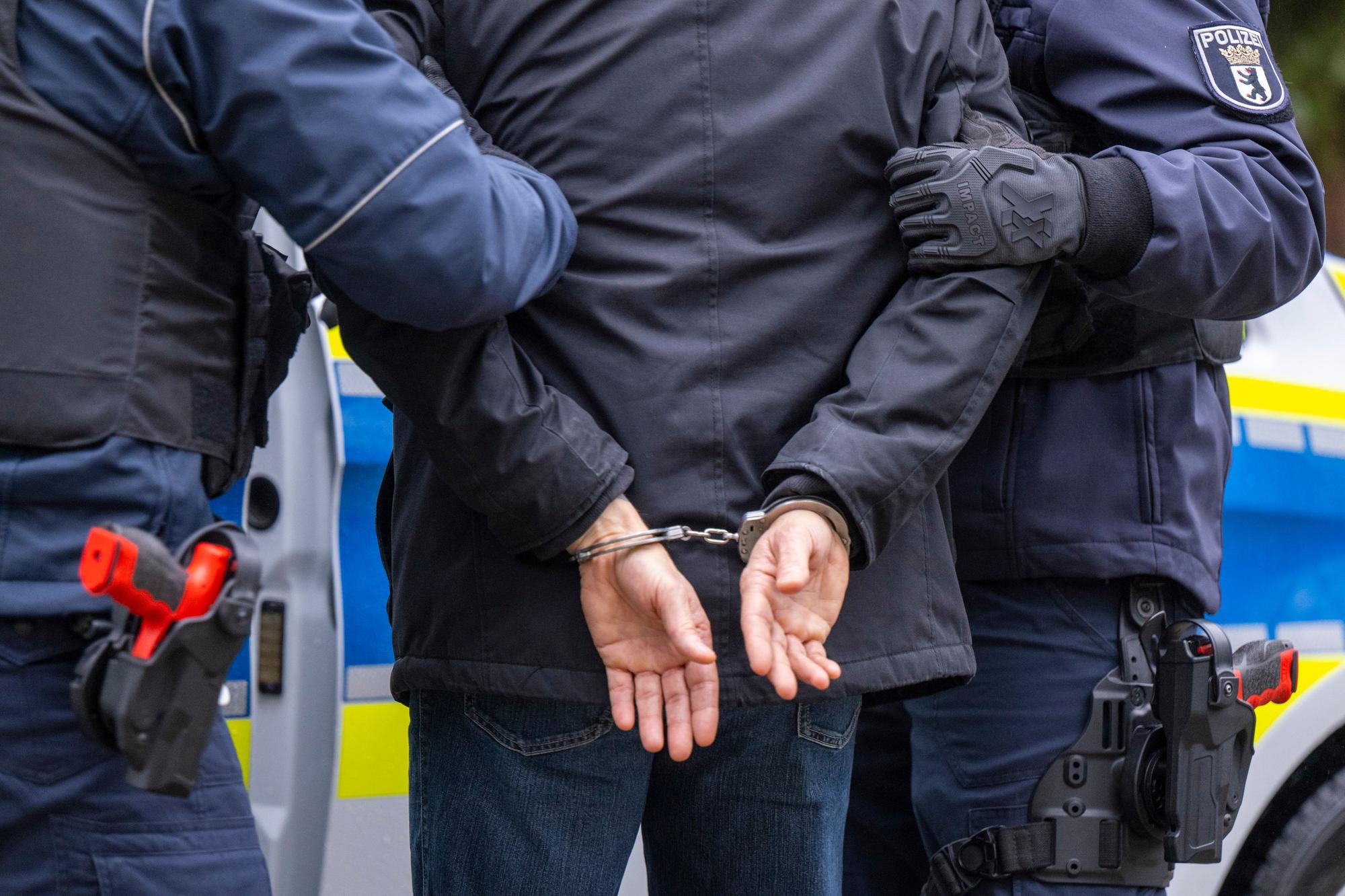 Polizisten nehmen einen Mann fest, der in Handschellen abgeführt wird.