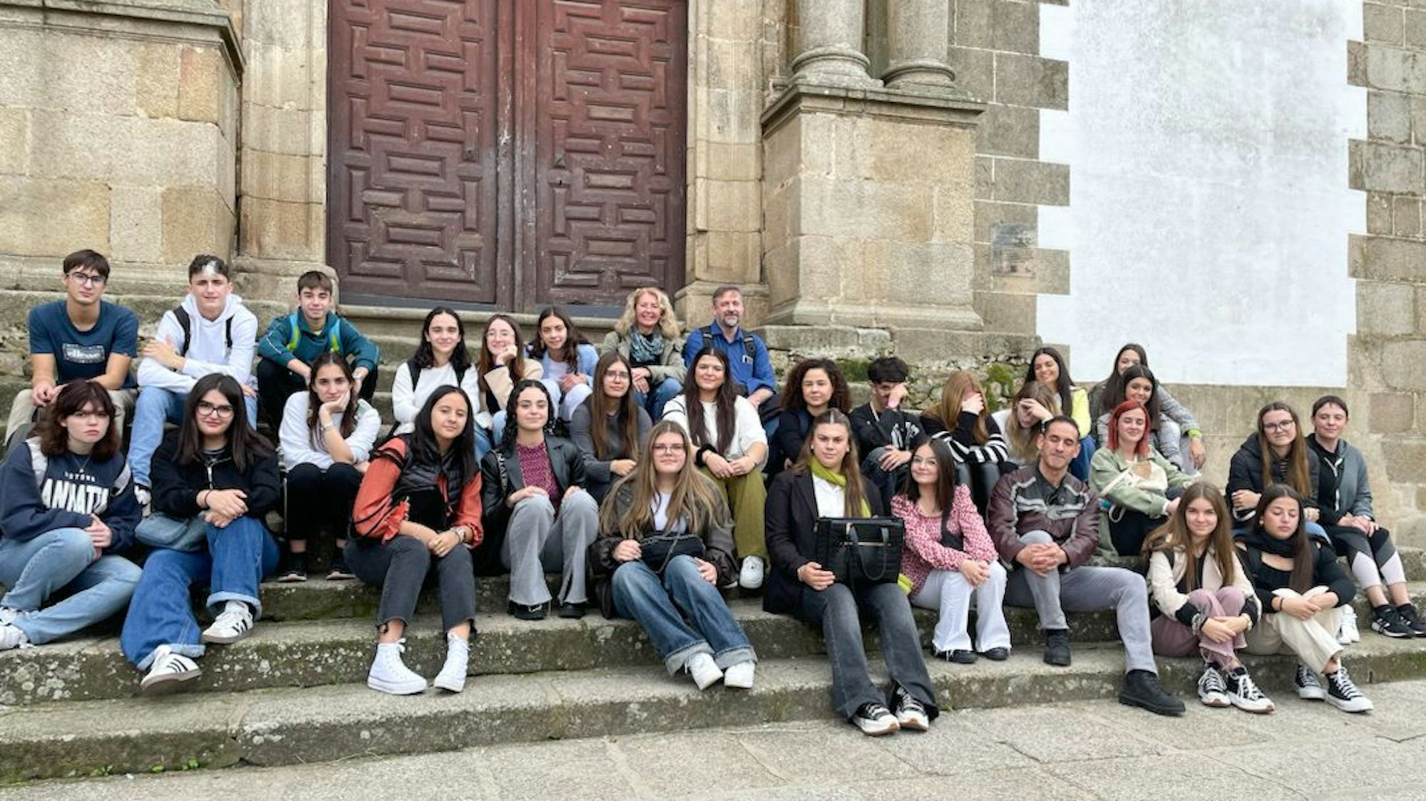 Schülerinnen und Schüler sitzen auf der Treppe vor einer Kirche in Spanien.