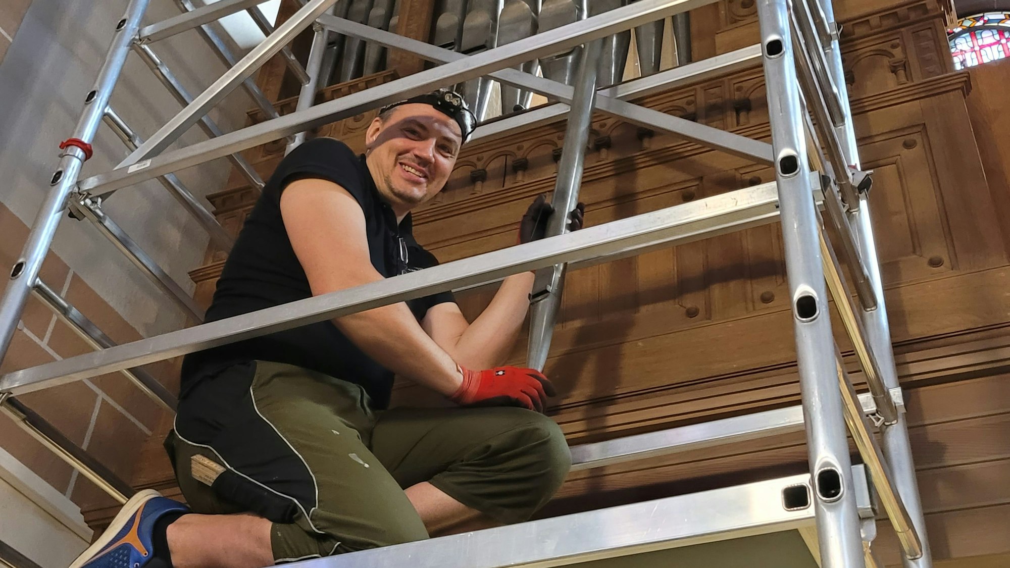 Der Orgelbauer Björn-Daniel Reich kniet auf einem meterhohen Gerüst, er bearbeitet die Pfeifen.