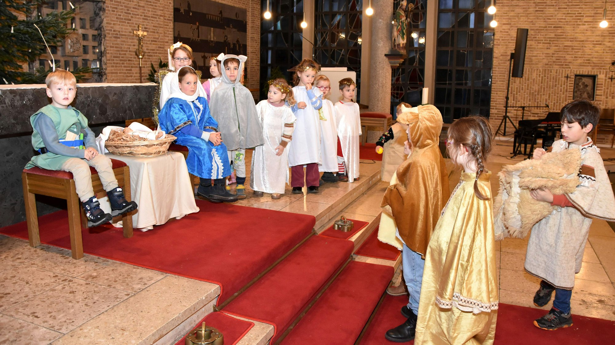 Auf dem Bild sind mehrere Kinder in Kostümen zu sehen, die in einer Kirche Jesu Geburt nachspielen. Zwischen Josef und Maria liegt Baby-Jesus in einem Korb.