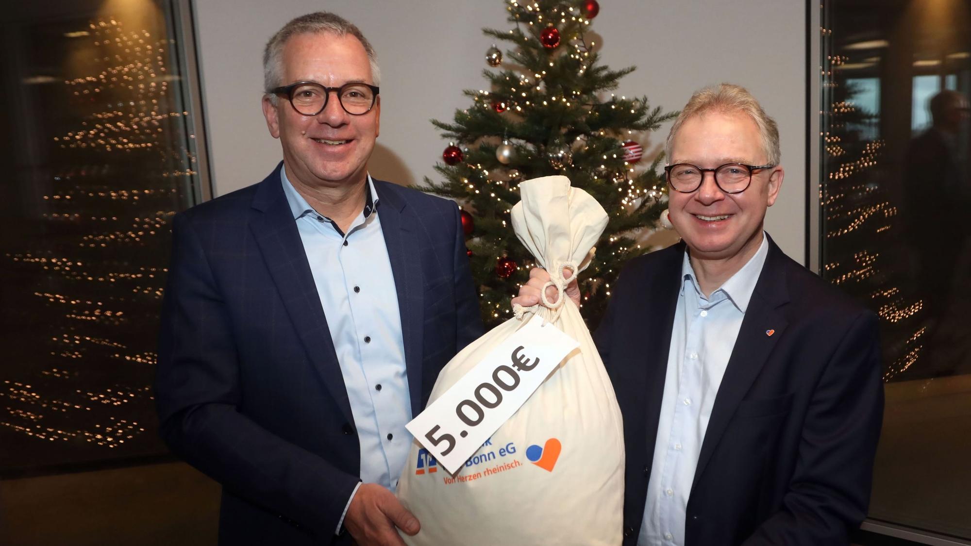 Christian Hümmeler (li.) freut sich über einen symbolischen Sack voller Geld für „wir helfen“ – überreicht von Jürgen Pütz, dem Vorstandsvorsitzenden der Volksbank Köln-Bonn.