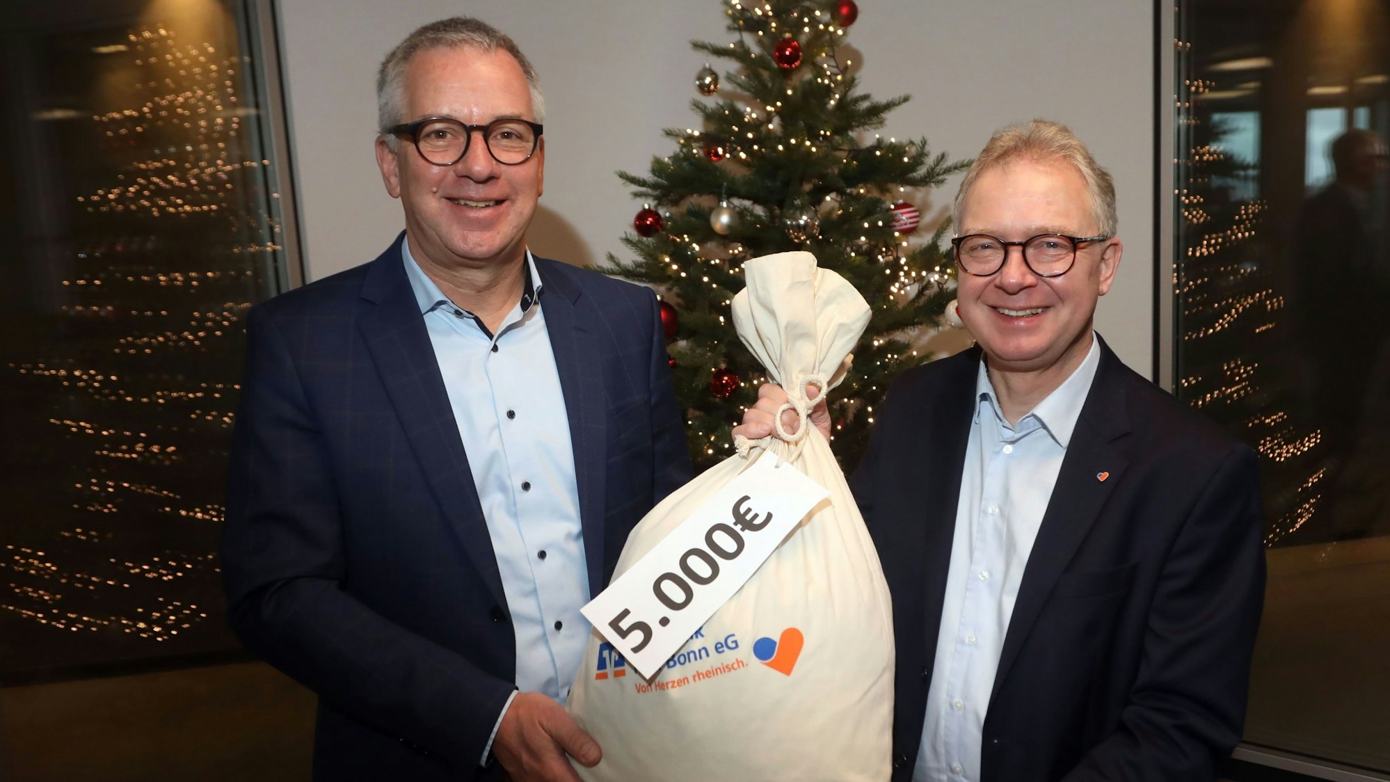 Christian Hümmeler (li.) freut sich über einen symbolischen Sack voller Geld für „wir helfen“ – überreicht von Jürgen Pütz, dem Vorstandsvorsitzenden der Volksbank Köln-Bonn.