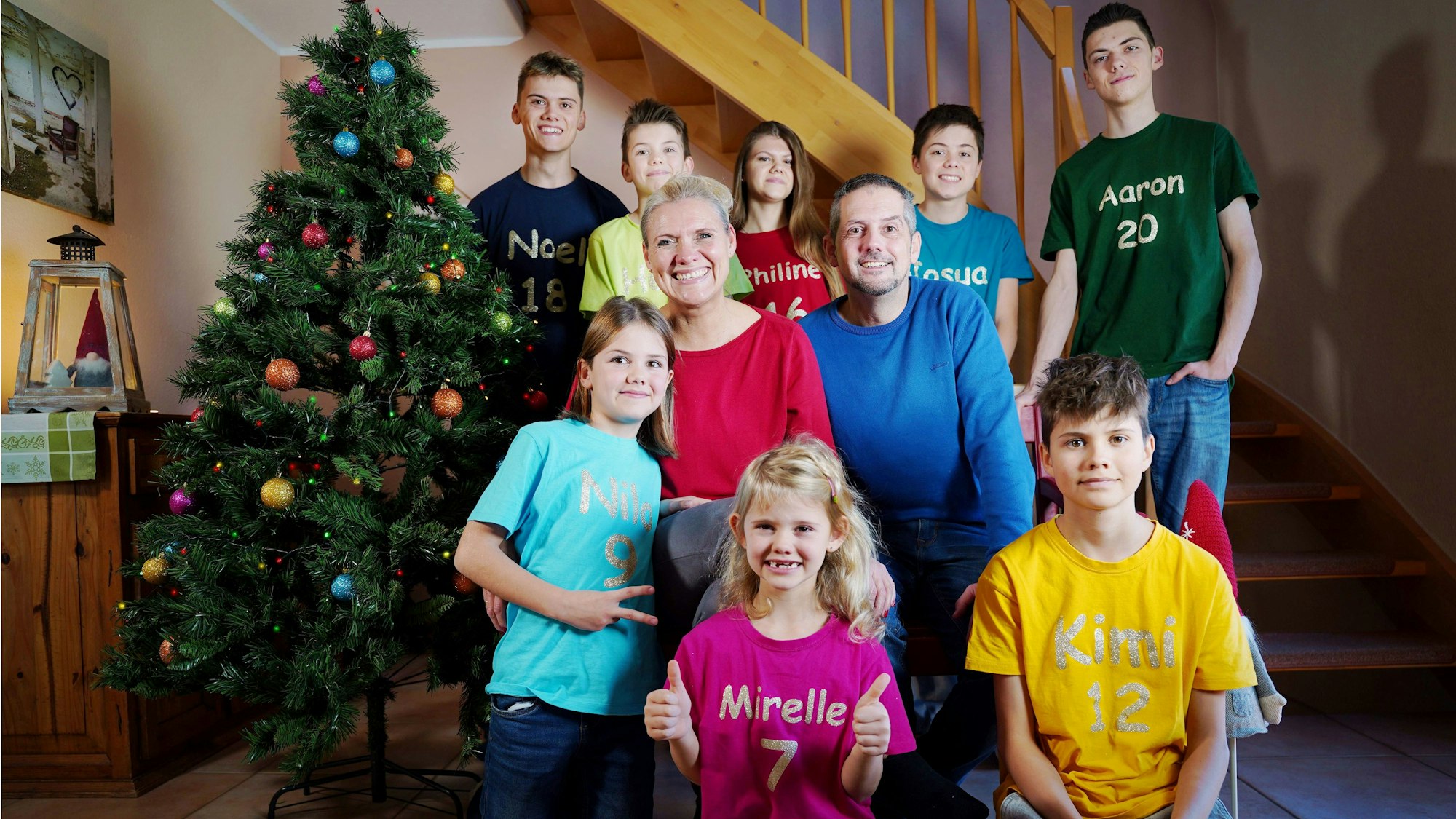 Katja und André Dederichs hocken neben einem Weihnachtsbaum. Vor und hinter ihnen sind ihre acht Kinder.