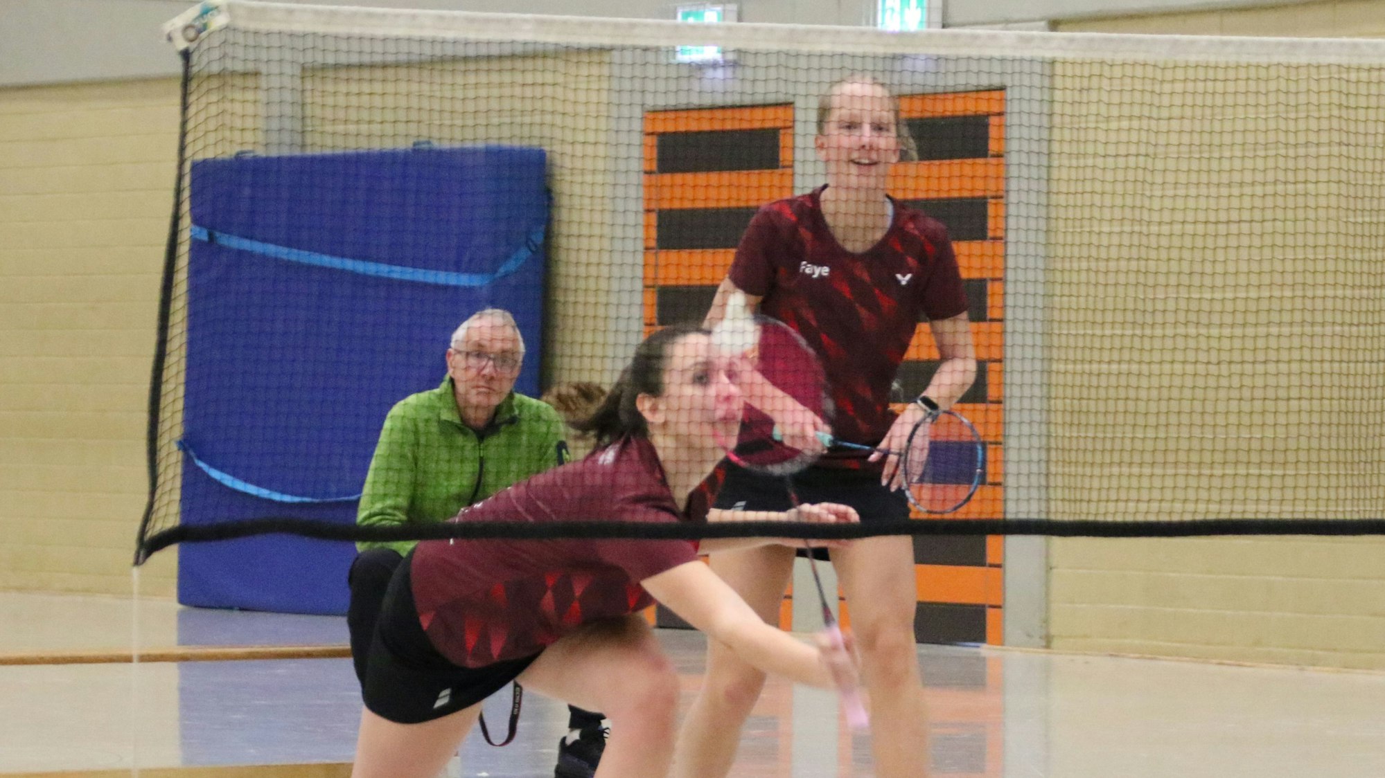 Nela-Sophie Wozny streckt sich, um einen Ball zu erreichen. Ihre Mitspielerin grinst. Dahinter sitzt ein Mann und schaut zu.