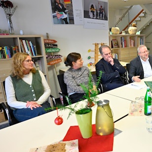 Eine Runde von Frauen und Männern sitzt an einem Tisch und bespricht sich.