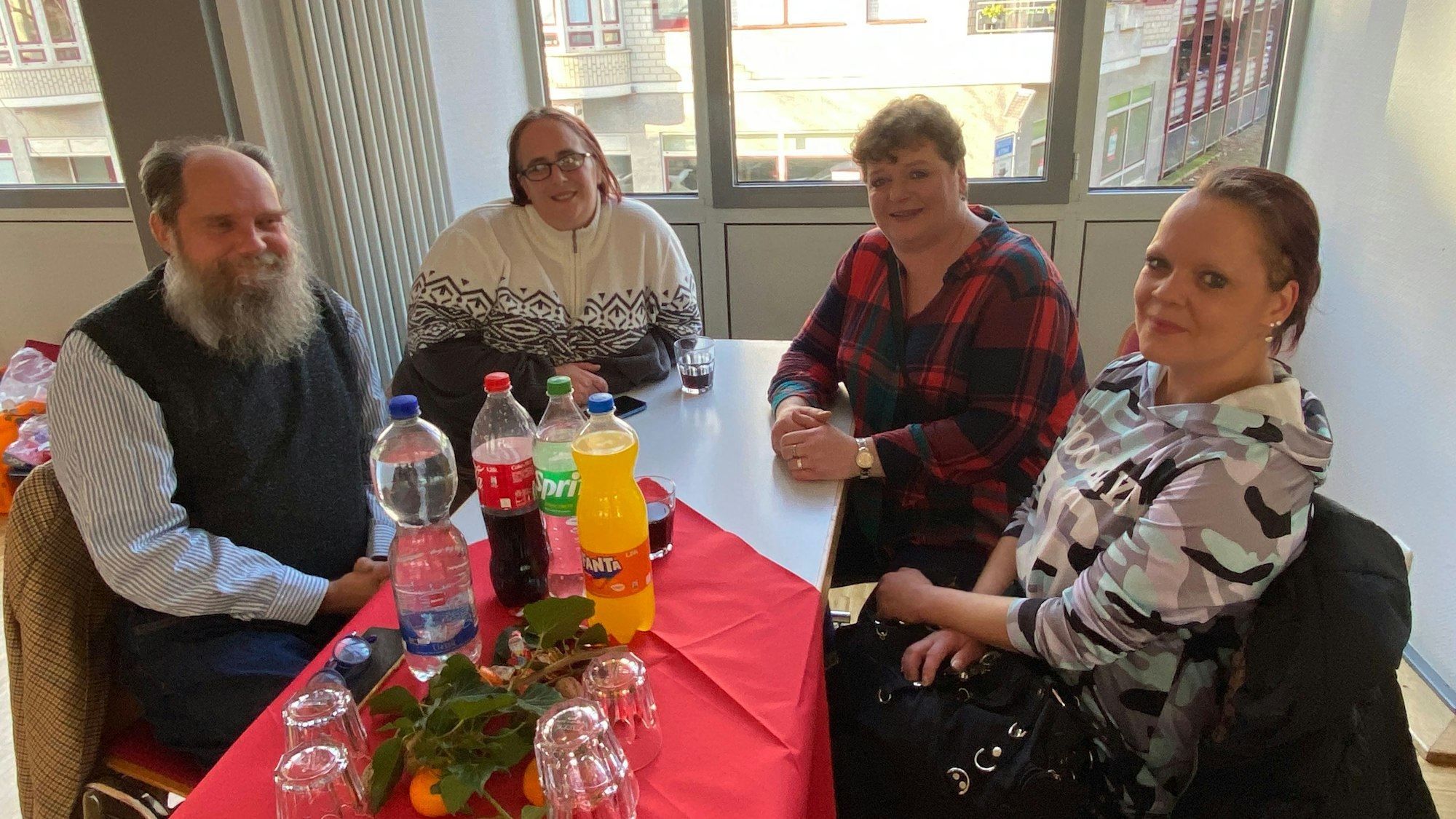 Ein Mann und drei Frauen sitzen an einem weihnachtlich dekorierten Tisch und blicken in die Kamera.