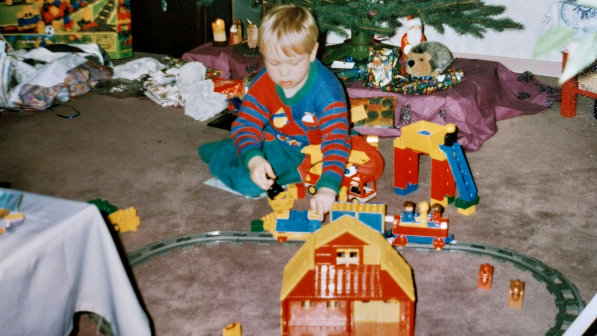 Ein Kind sitzt unter dem Tannenbaum und spielt mit einer Lego-Eisenbahn.