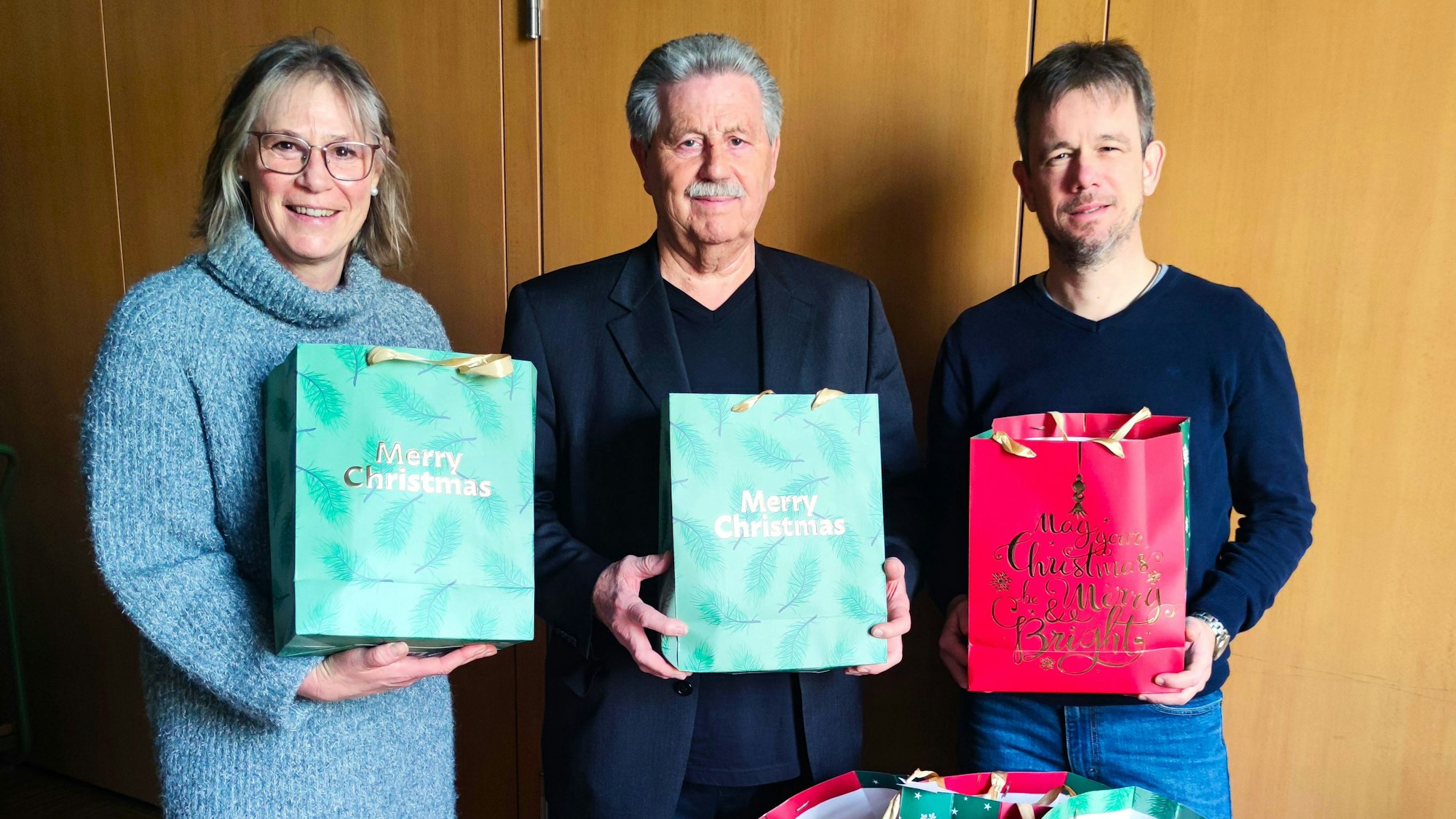 Eine Frau und zwei Männer halten vollgepackte Geschenketüten in ihren Händen.