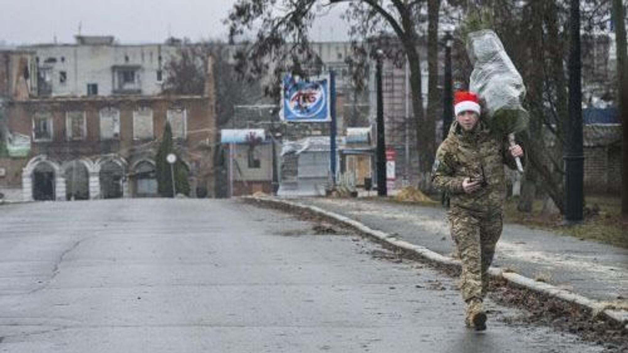 Ein ukrainischer Soldat mit Weihnachtsmütze trägt einen Tannenbaum durch eine Straße der Region Charkiw.