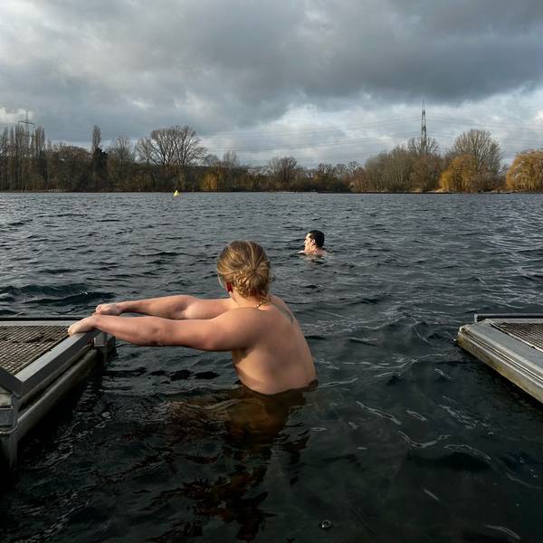 Zwei junge Männer gehen im Fühlingersee im Winter baden. Der Himmel ist mit dunklen Wolken behangen.