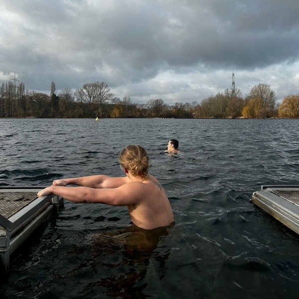 Zwei junge Männer gehen im Fühlingersee im Winter baden. Der Himmel ist mit dunklen Wolken behangen.