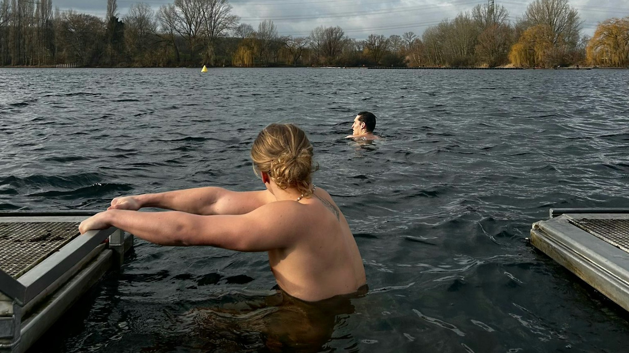 Zwei junge Männer gehen im Fühlingersee im Winter baden. Der Himmel ist mit dunklen Wolken behangen.