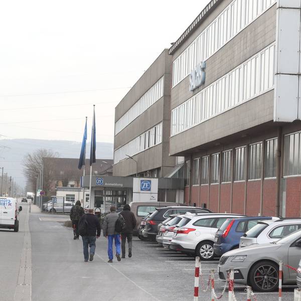 Menschen gehen an einem Industriegebäude vorbei.