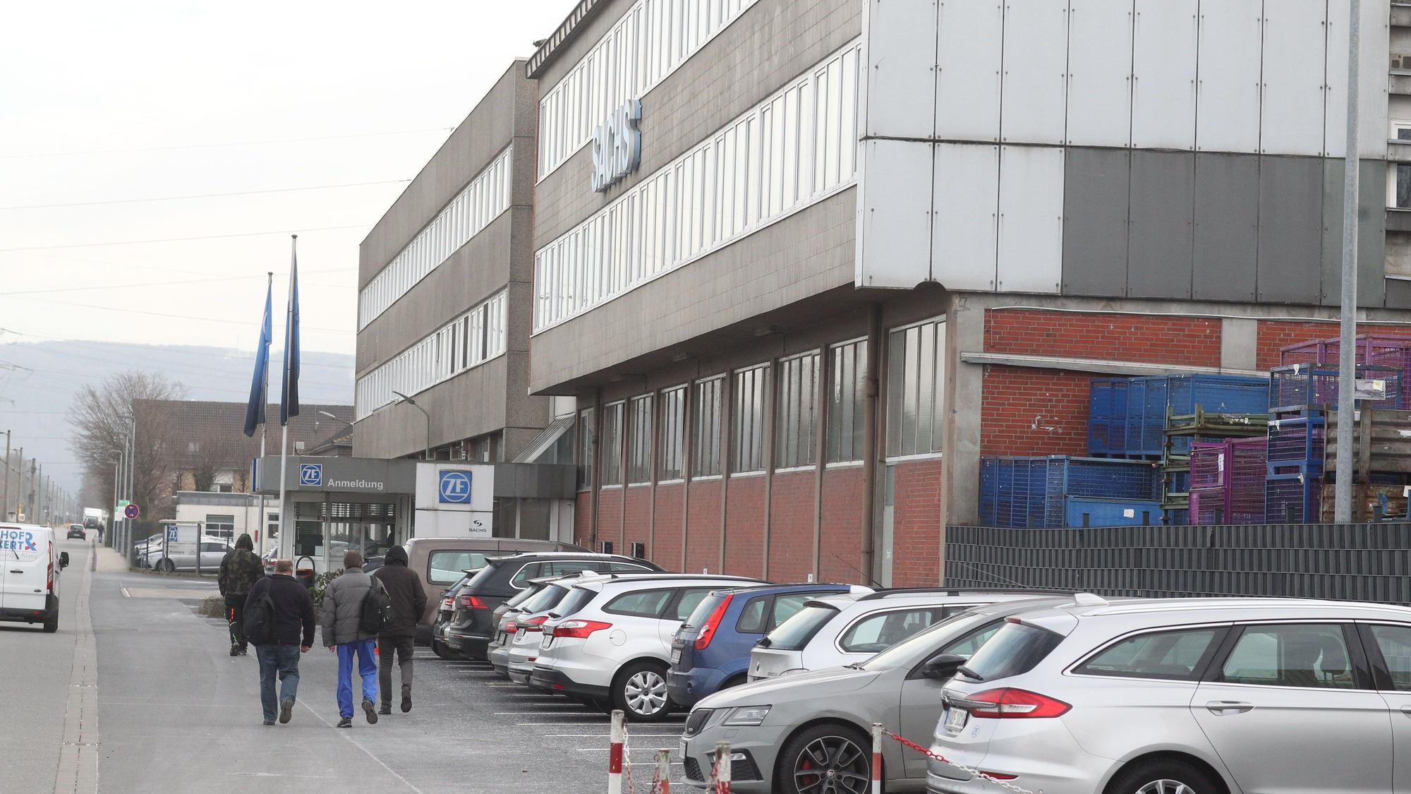 Menschen gehen an einem Industriegebäude vorbei.