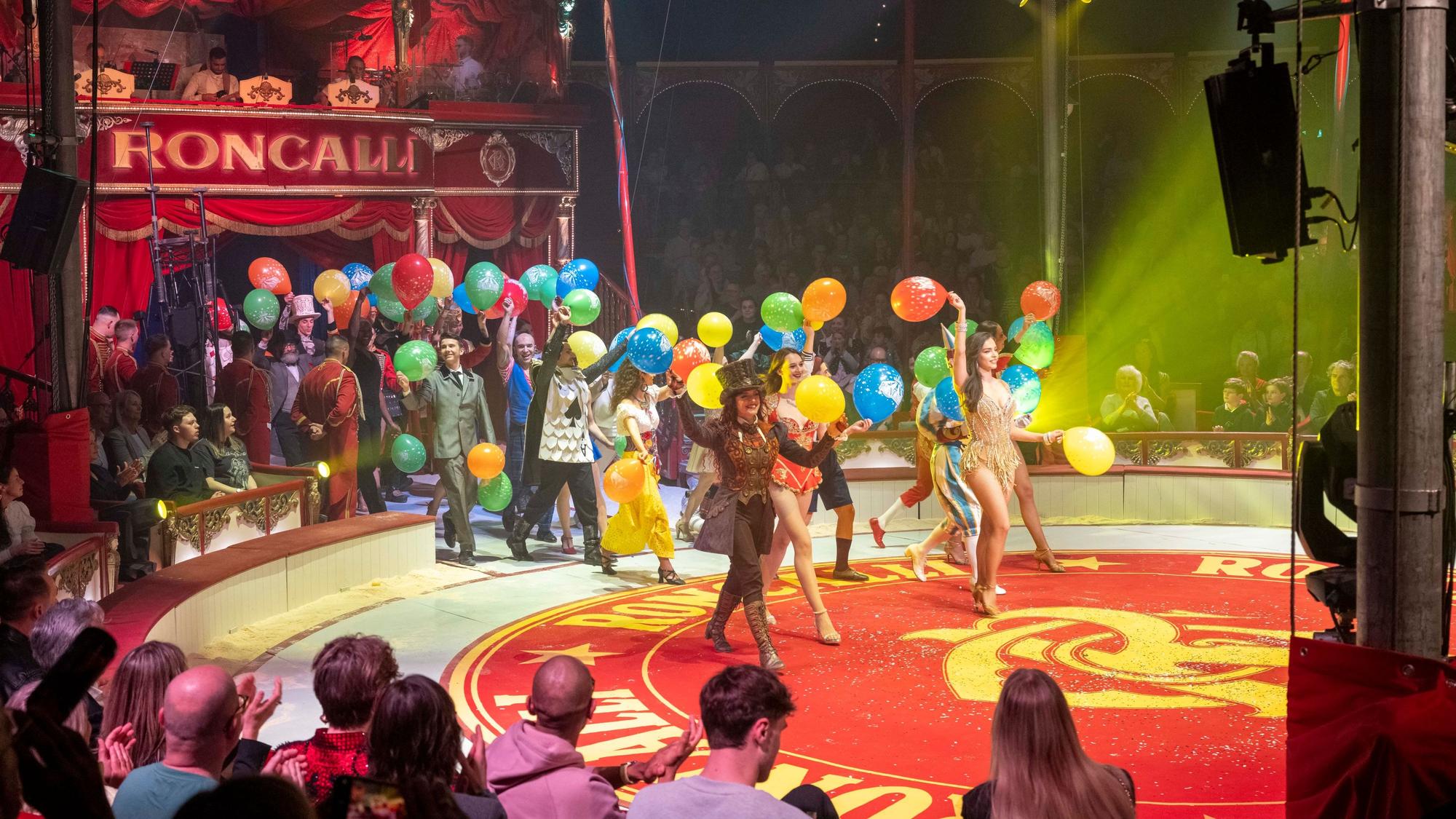 Artisten laufen zum Schluss-Applaus mit Luftballons in die Manege.