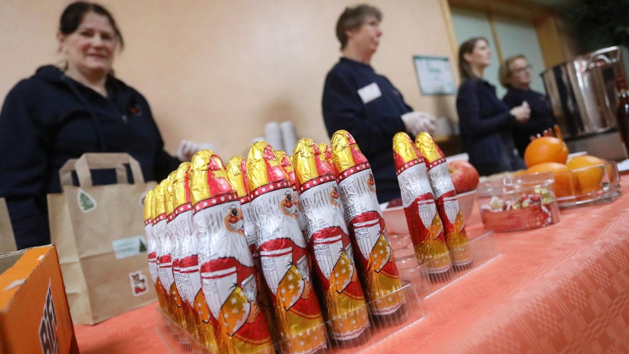 DRK-Helferinnen stehen hinter einem Tisch, auf dem unter anderen Schoko-Nikoläuse stehen.