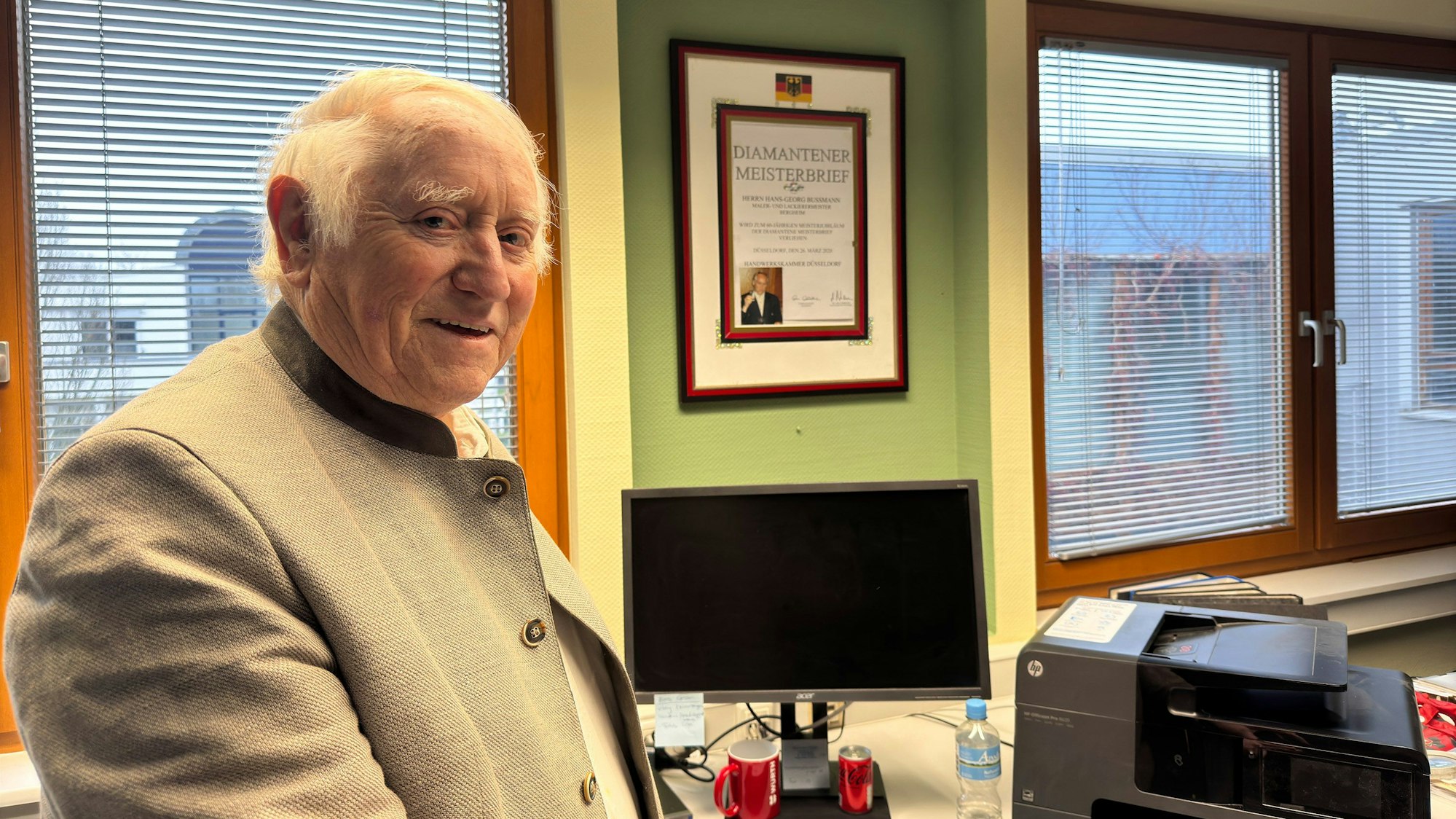 Ein Mann steht in seinem Büro vor seinem Diamantenen Meisterbrief.