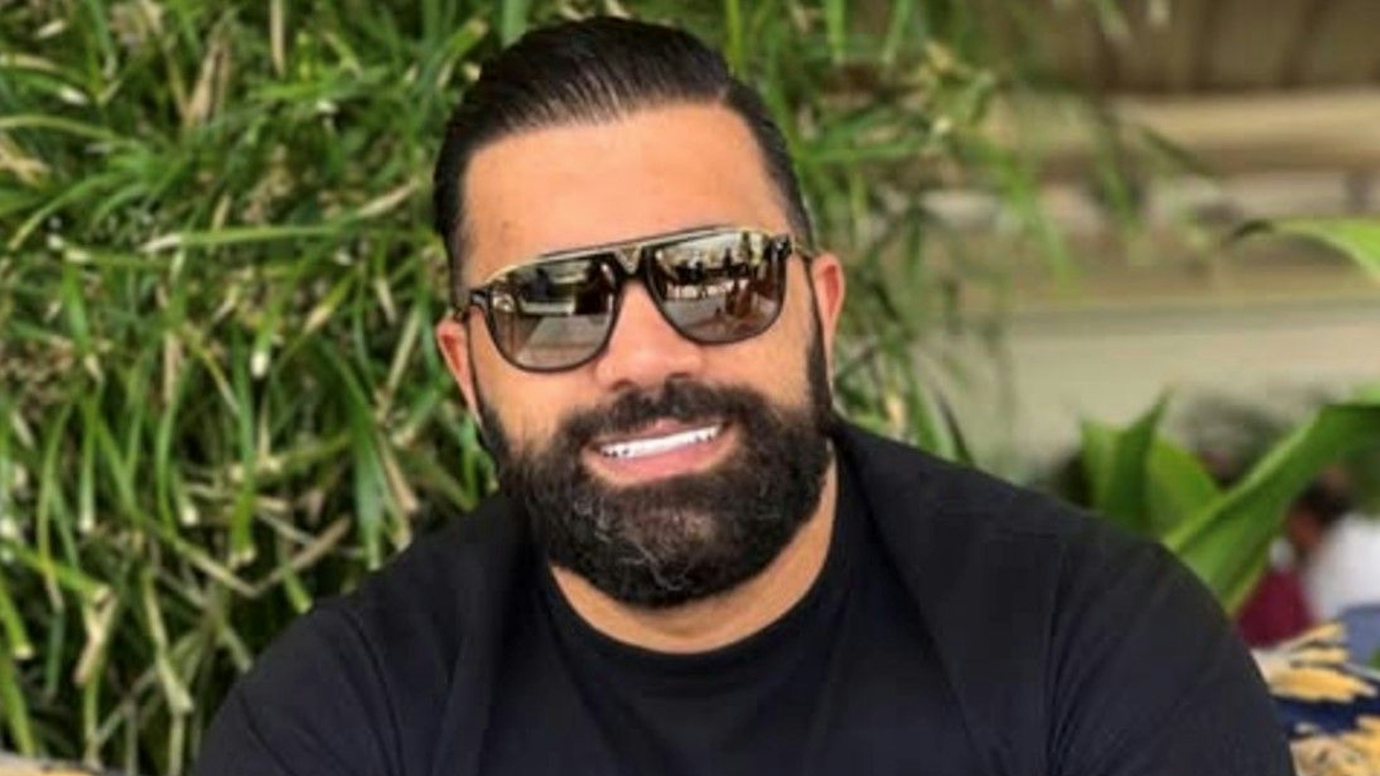 Ramin Y. ist mit Sonnenbrille und Bart zu sehen. Er trägt ein schwarzes T-Shirt und eine goldene Rolex auf komplett tätowierten Armen.