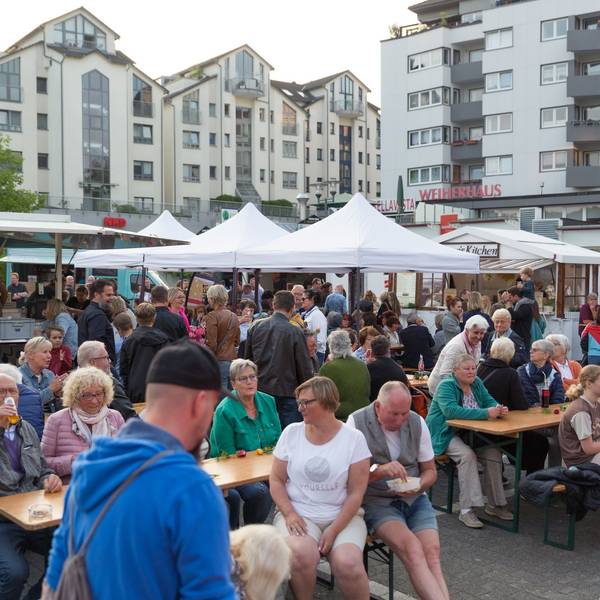 Menschen sitzen auf Bierbänken vor Pavillons.