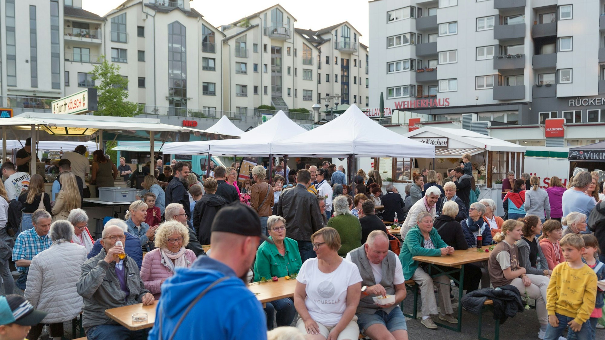 Menschen sitzen auf Bierbänken vor Pavillons.