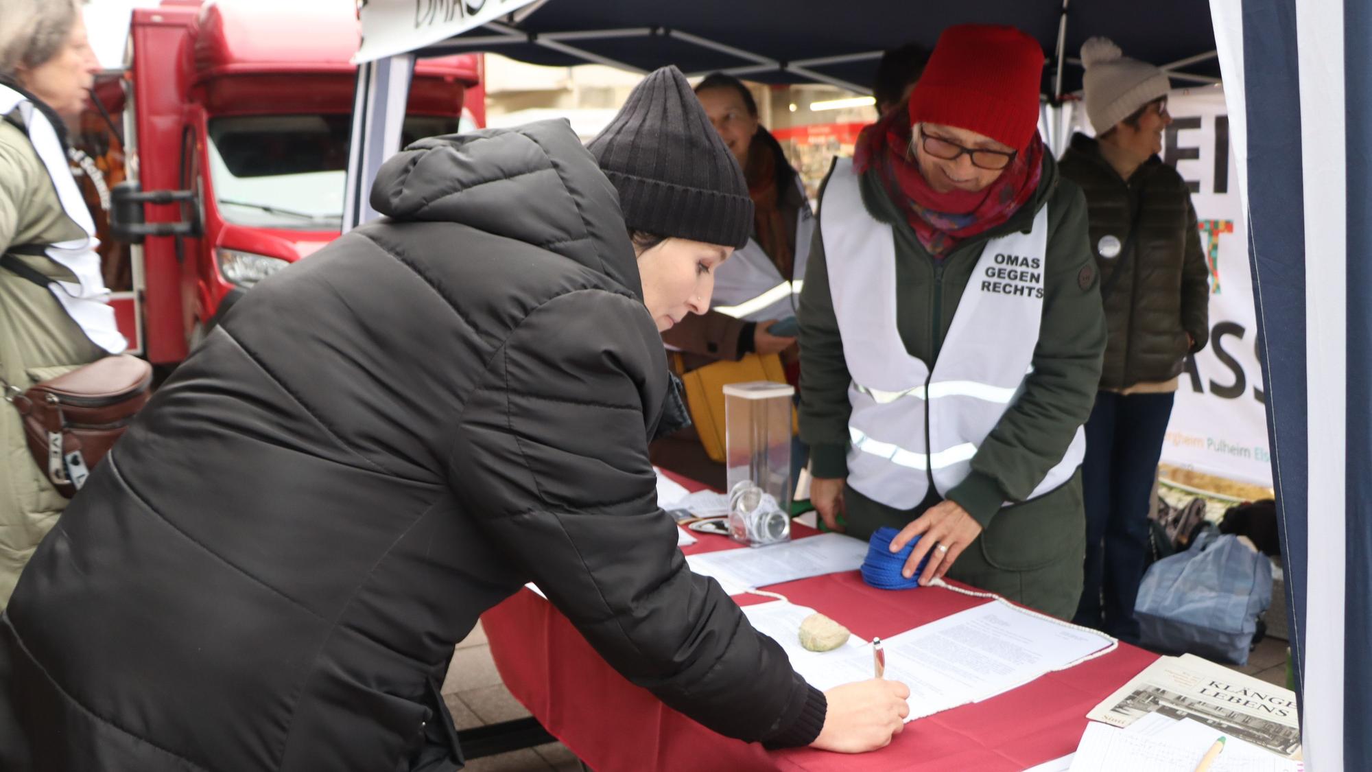 Das Foto zeigt, wie eine junge Frau am Infostand der „Omas gegen Rechts“ Brühl einen Zettel unterschreibt.
