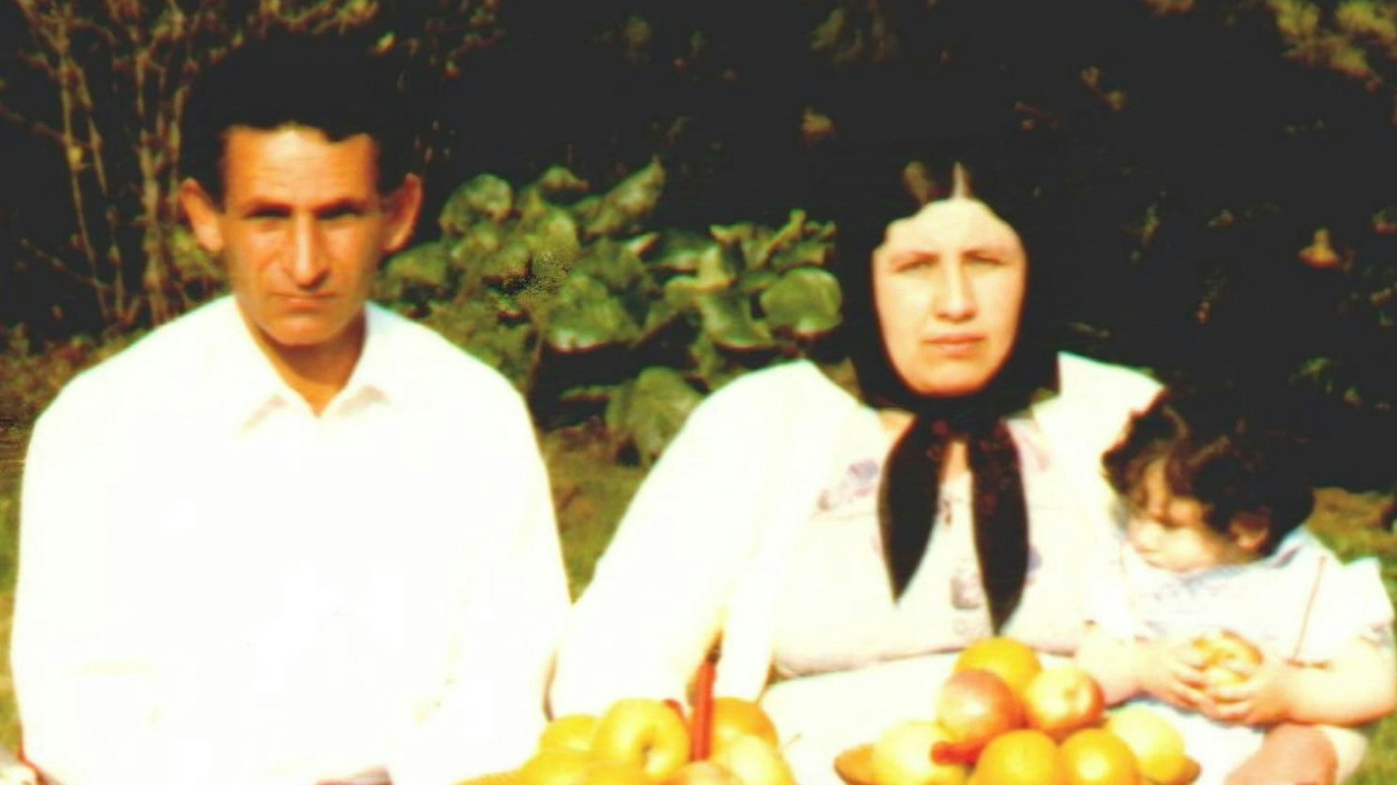 Das Bild zeugt das Paar in einem Garten sitzend, die Frau hält ihre kleine Tochter. Auf dem Tisch vor ihnen sind Äpfel.