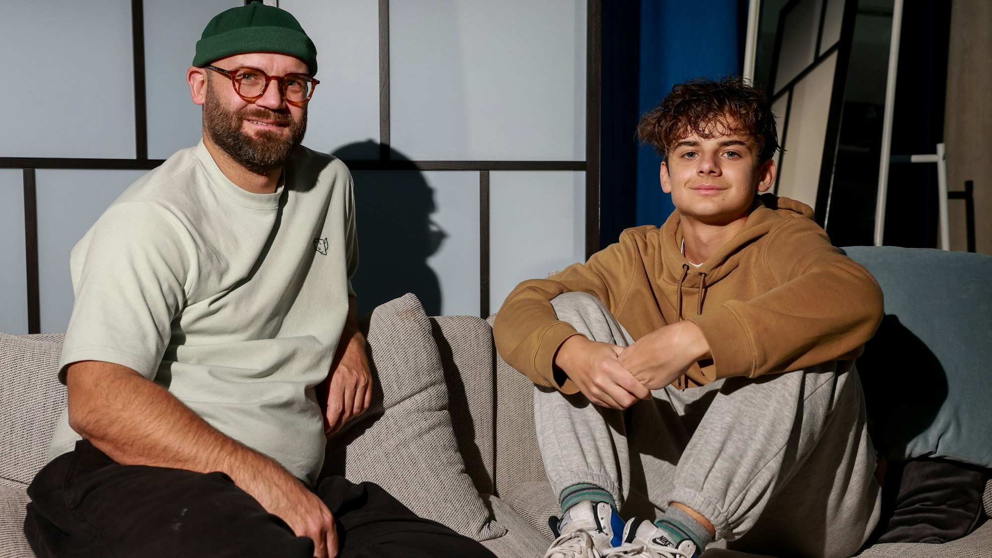 Asterios Rose und sein Vater Thorsten Rose sitzen nebeneinander und lächeln.