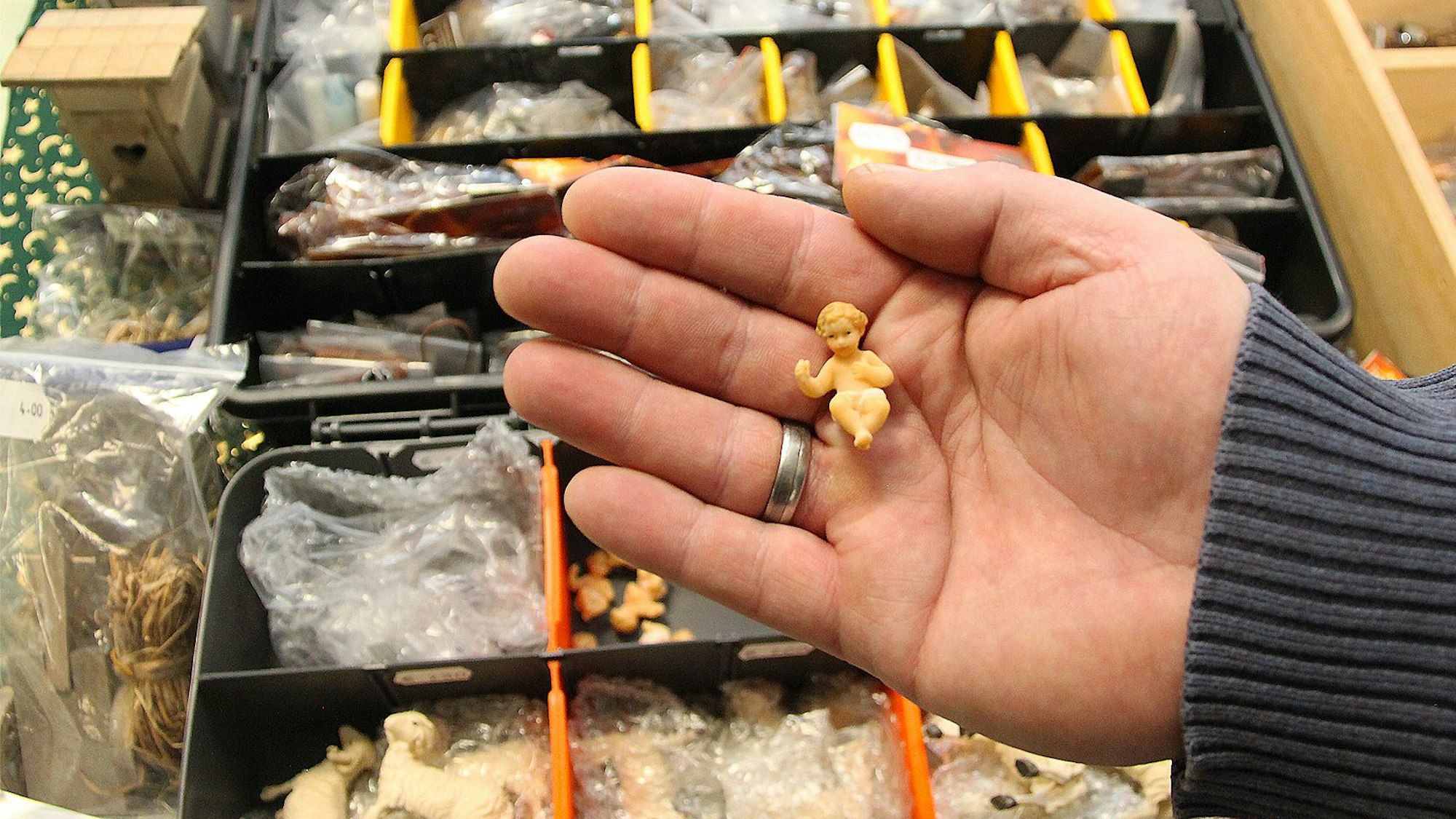Ein Mann hält die winzig kleine Figur eines Jesuskindes für eine Krippendarstellung in der Hand.