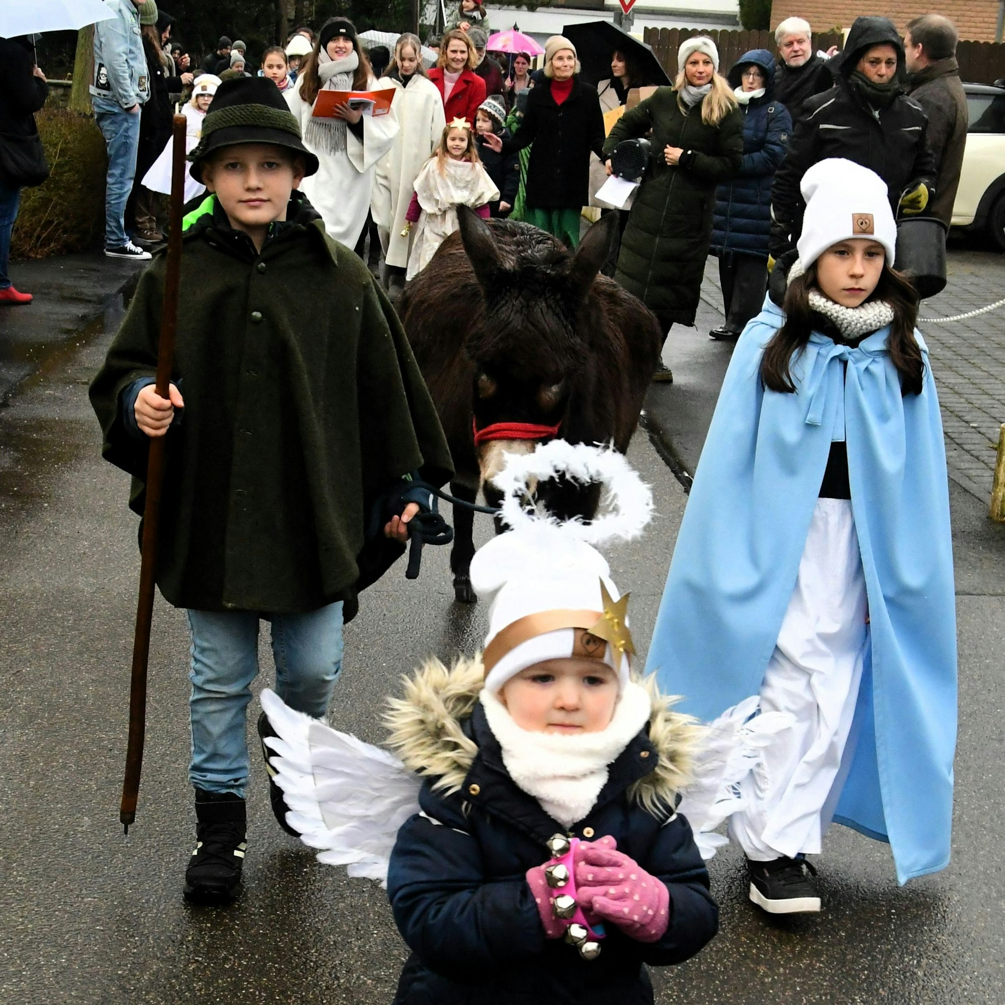 Drei Kinder stellen bei einem Krippenspiel einen Engel, Maria und Josef dar. Sie führen auch einen Esel.