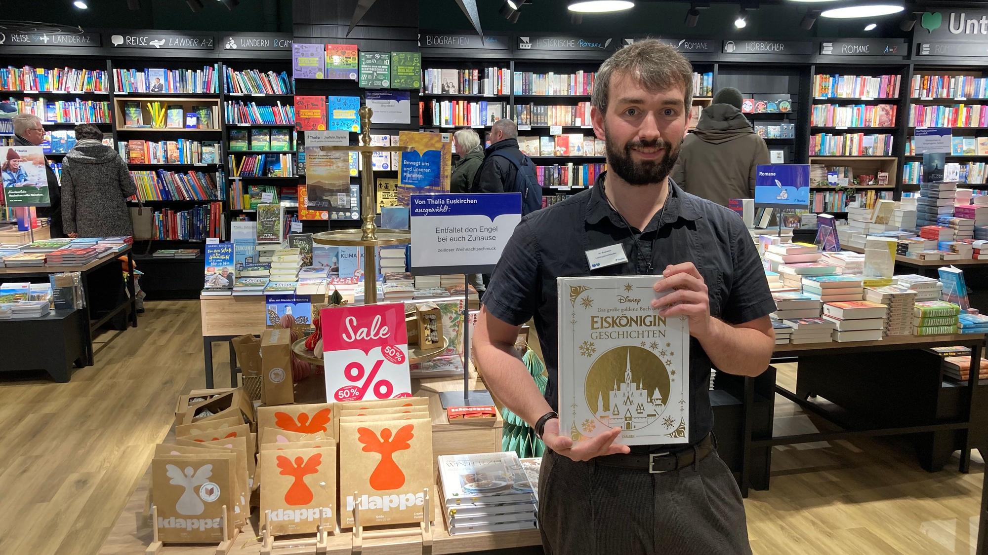Ein Mann hält ein Buch vor sich. Er steht in einem Buchladen vor reduzierten Artikeln.
