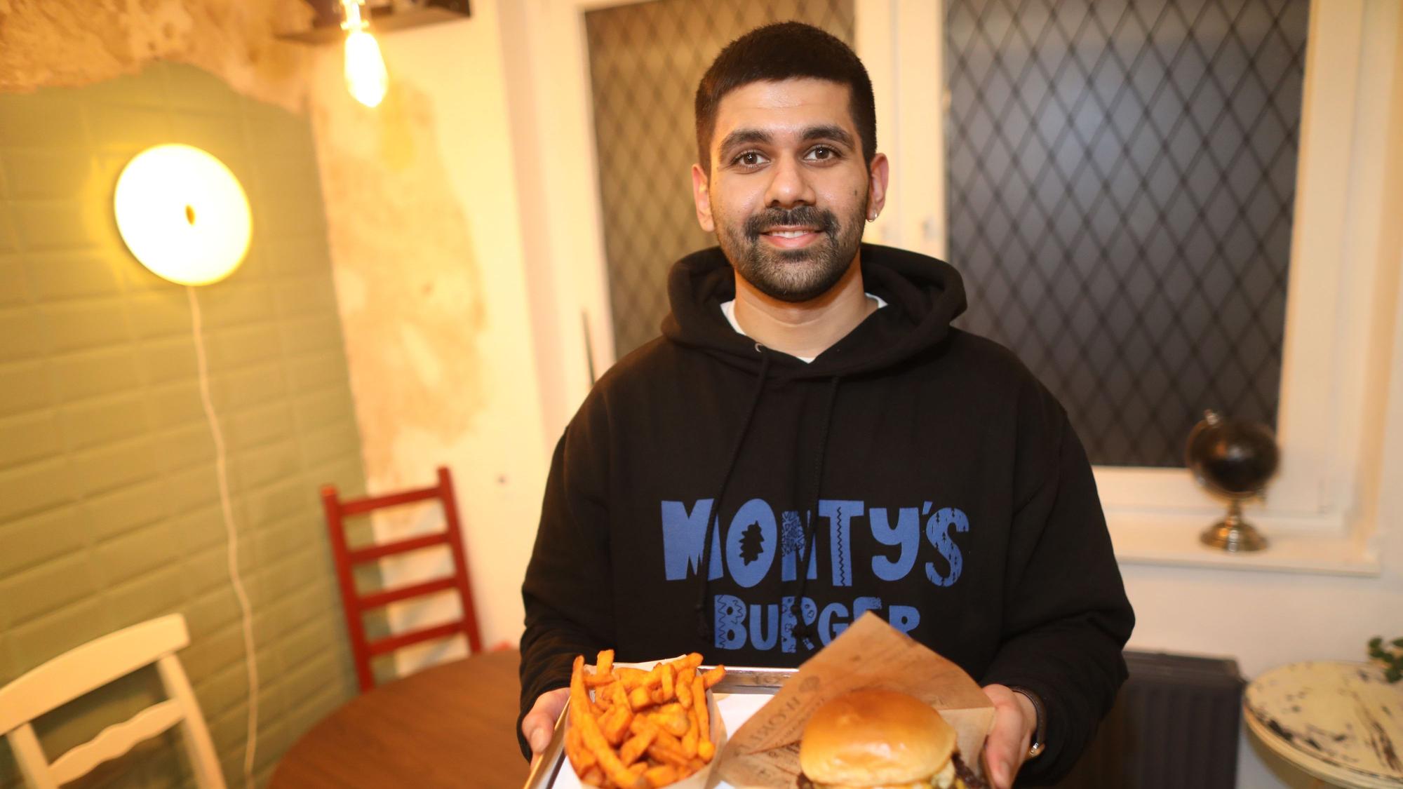 Inhaber Mandip Singh ist mti einem Tablett voll Burger und Fritten zu sehen.